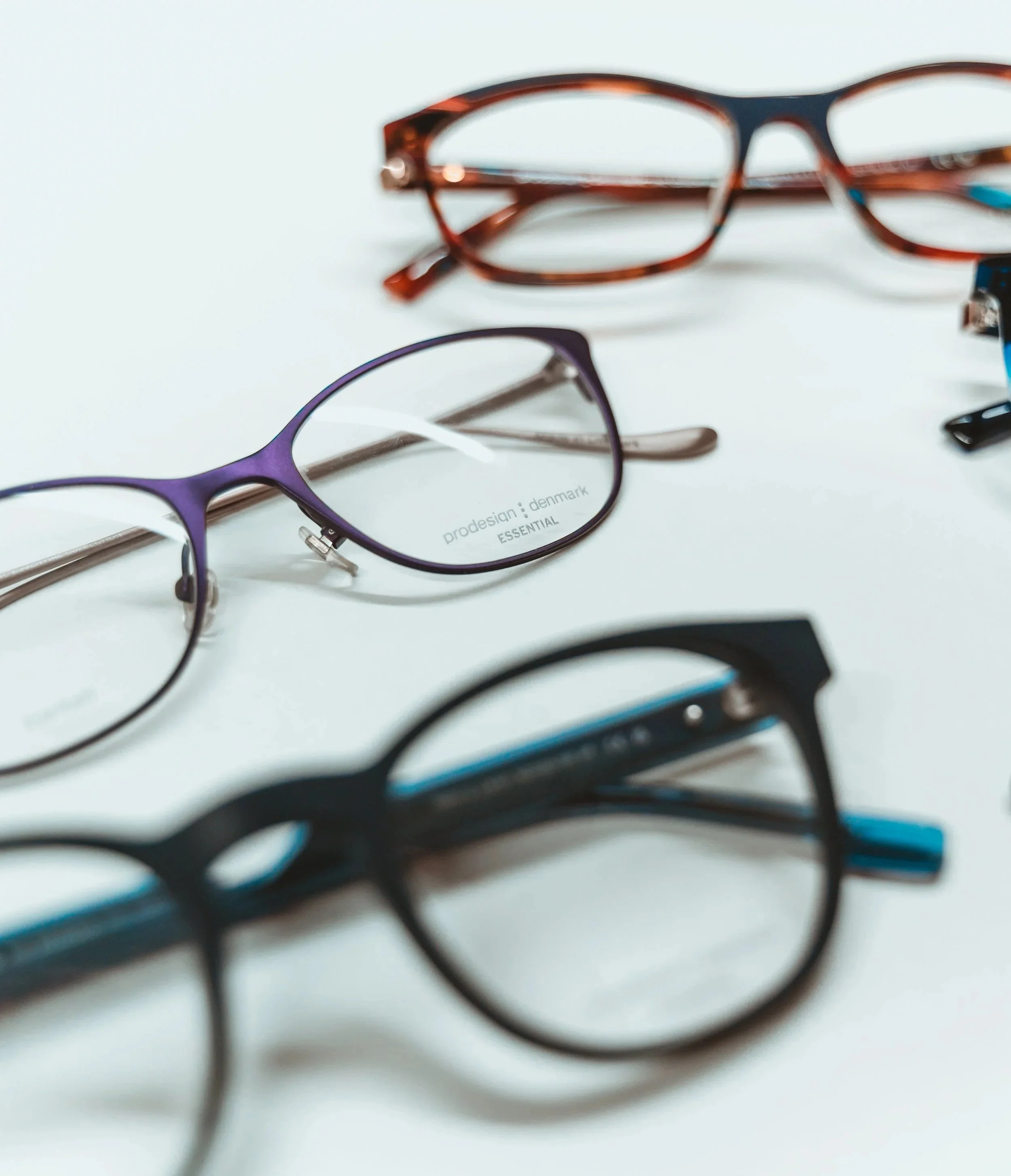 Close-up of three pairs of eyeglasses on a white surface, with one pair in focus and others blurred.