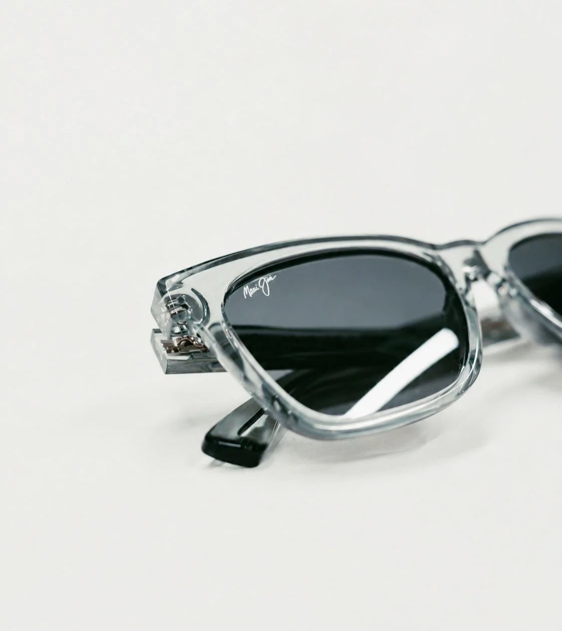 Close-up of a pair of clear-framed sunglasses with dark lenses, placed on a white surface.