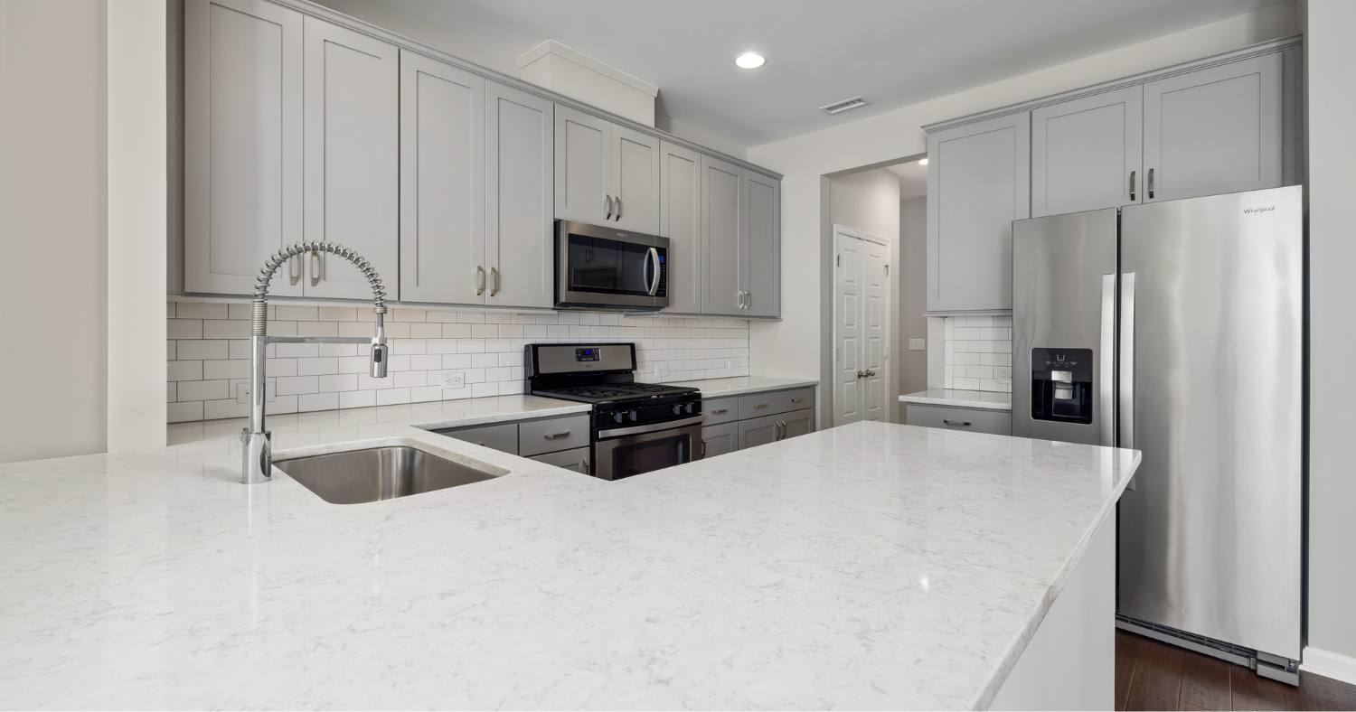 Modern kitchen with gray cabinets, white marble countertops, stainless steel appliances, and a white subway tile backsplash.