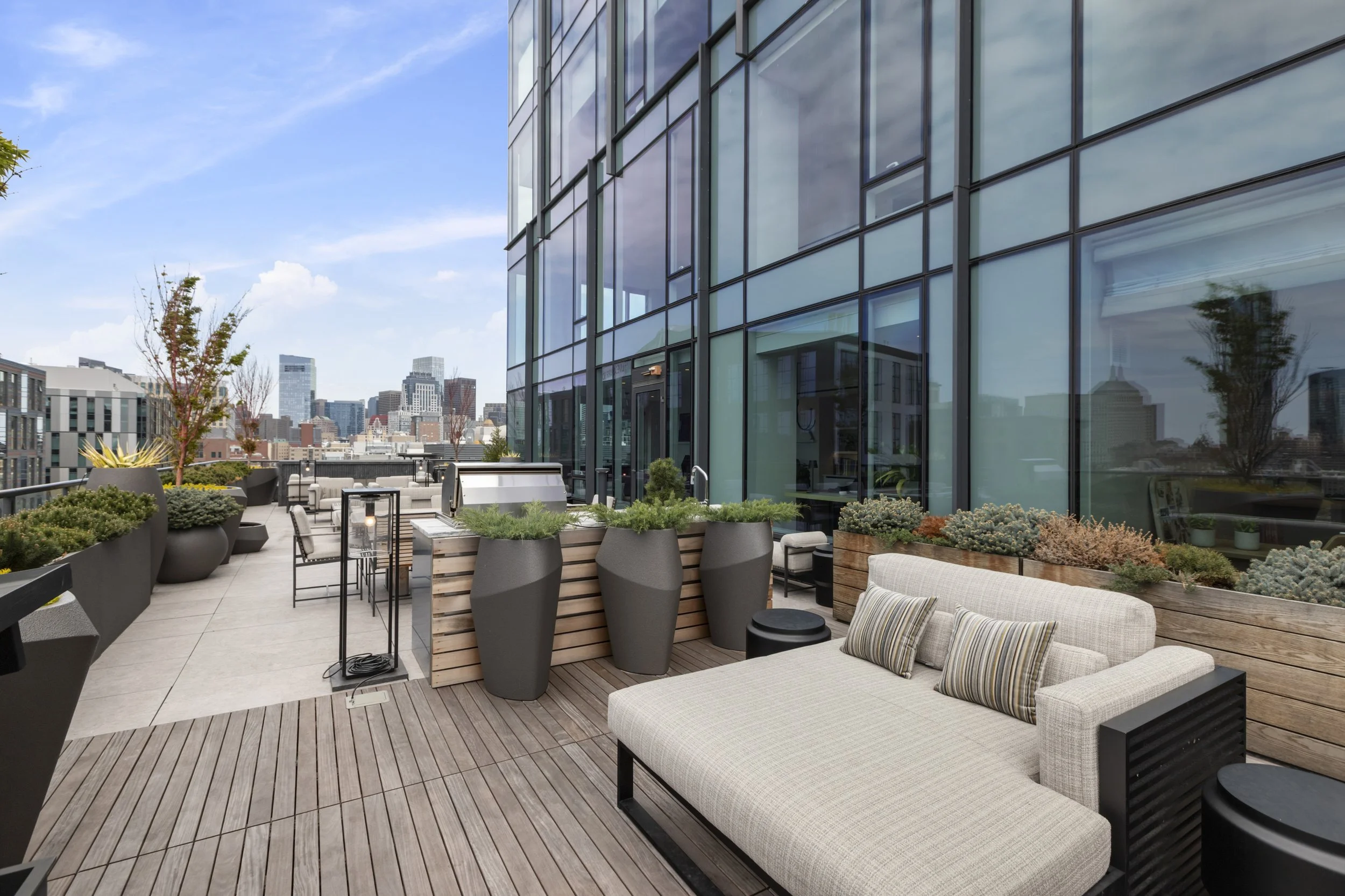 Rooftop terrace with outdoor seating, potted plants, and city skyline view in the background.