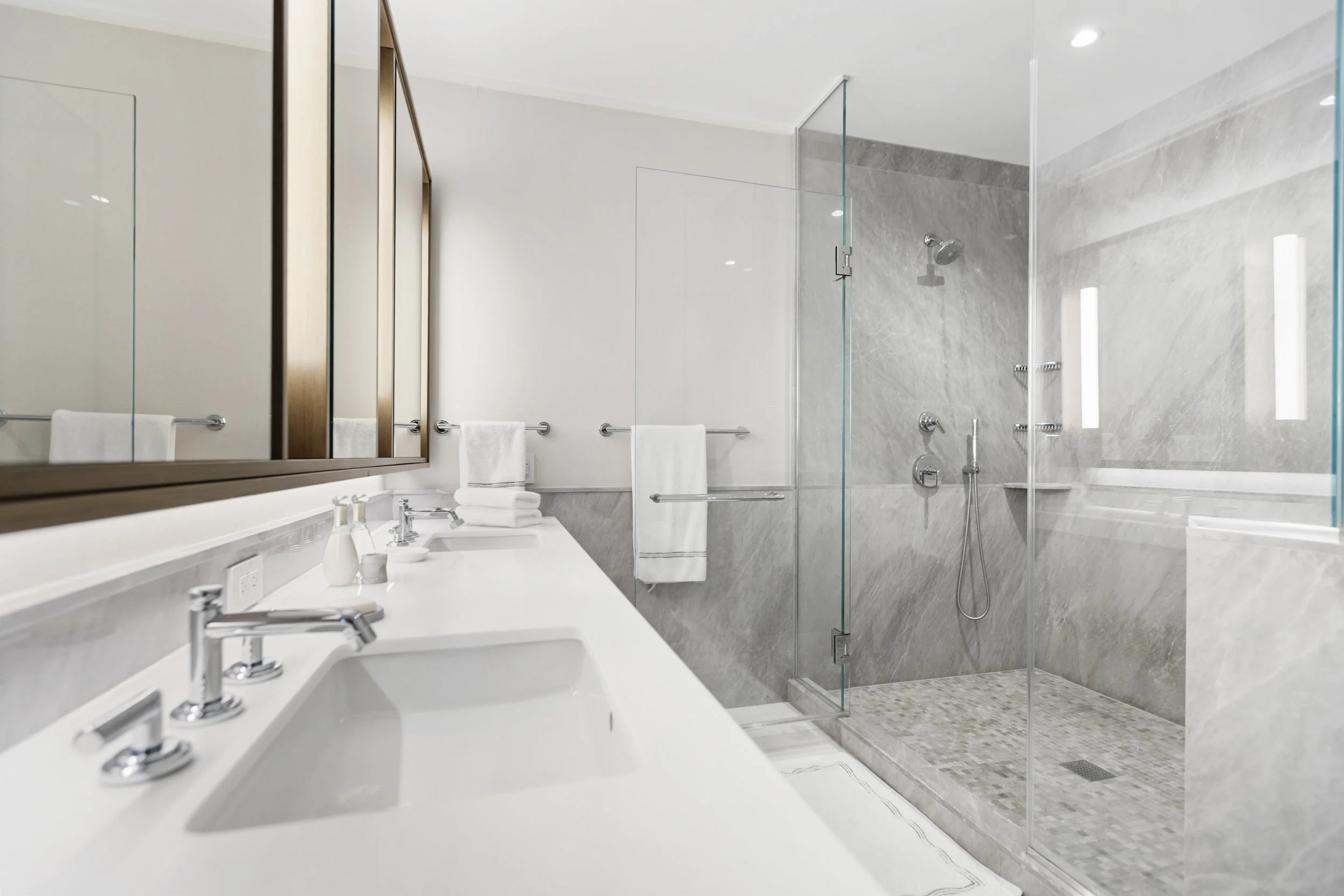 Modern bathroom with a double vanity sink, mirror, towel rack, and a separate glass-enclosed shower with a rainfall showerhead and wall-mounted fixtures.