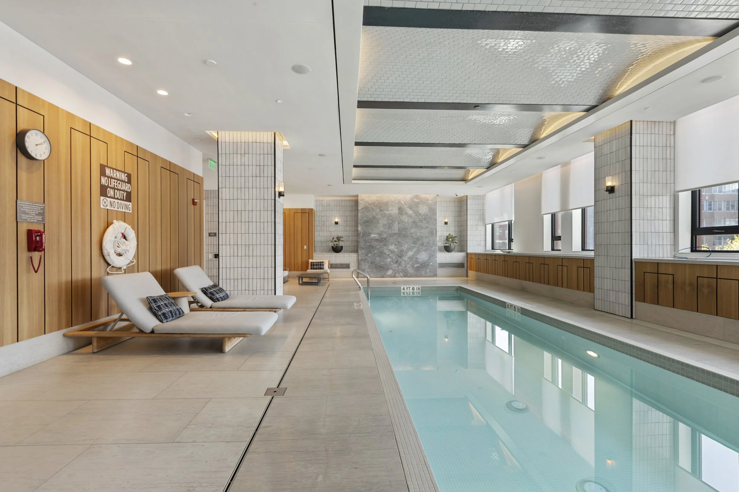 Indoor swimming pool area with lounge chairs, large windows, and modern decor.