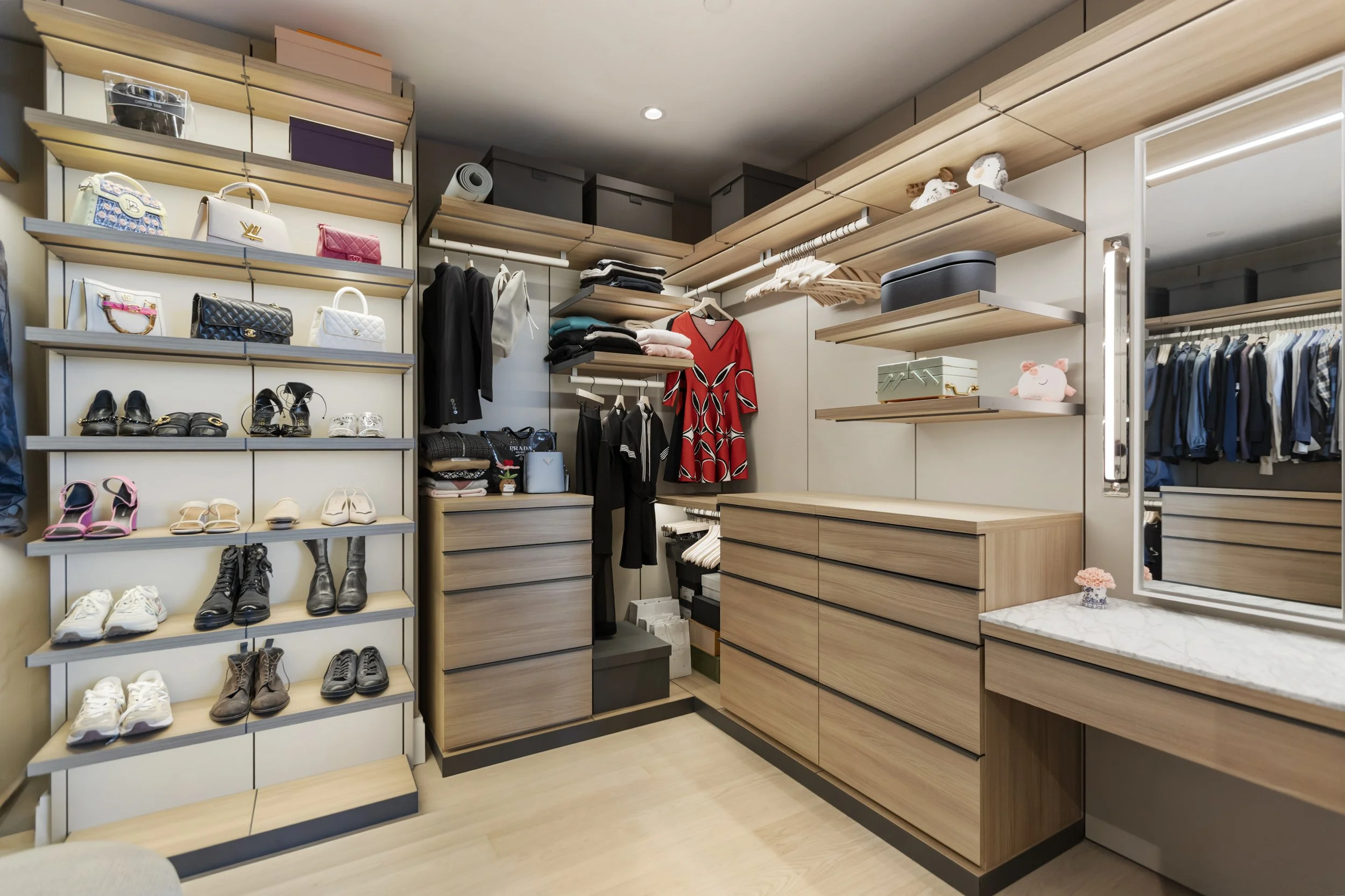 A walk-in closet with wooden shelves and drawers, displaying handbags, shoes, clothing, and storage boxes.