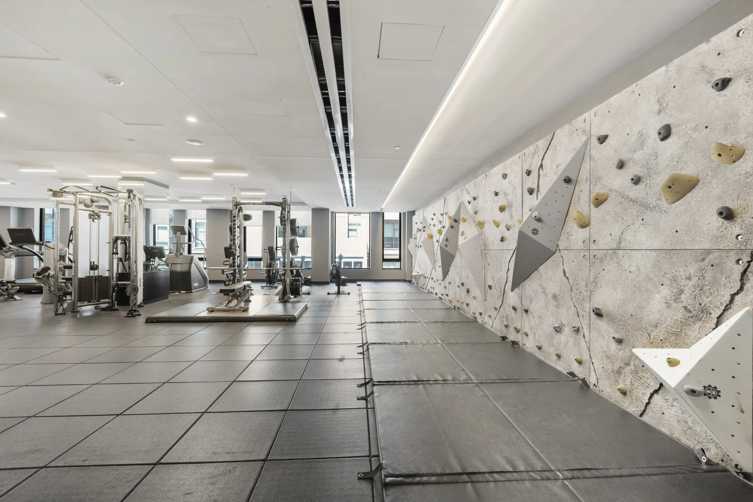 Interior of a modern gym with workout equipment, treadmills, and a rock climbing wall on the right side.