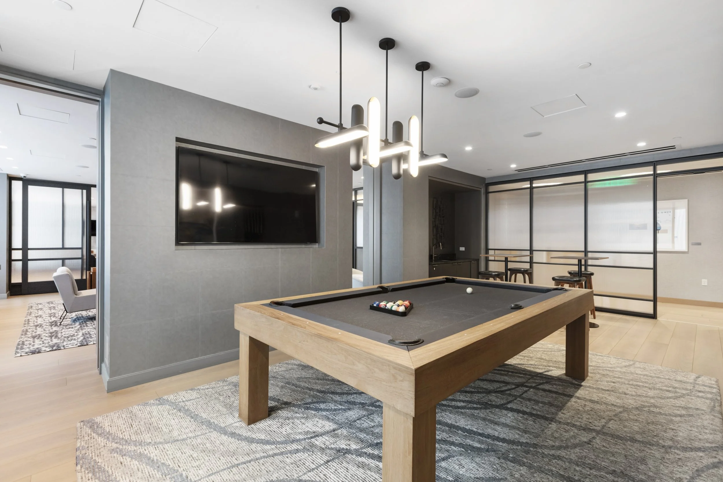 Modern lounge with a pool table, flat-screen TV, and stylish lighting fixtures in a spacious, well-lit room.
