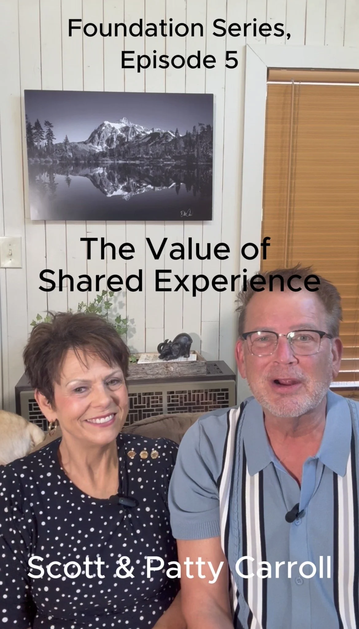 Two people, Scott and Patty Carroll, sitting together and smiling for a selfie in a room with white wall paneling. Behind them, there is a framed picture of a mountain reflection in a lake and a wooden window blind. The text overlay reads 'Foundation Series, Episode 5 The Value of Shared Experience Scott & Patty Carroll.'