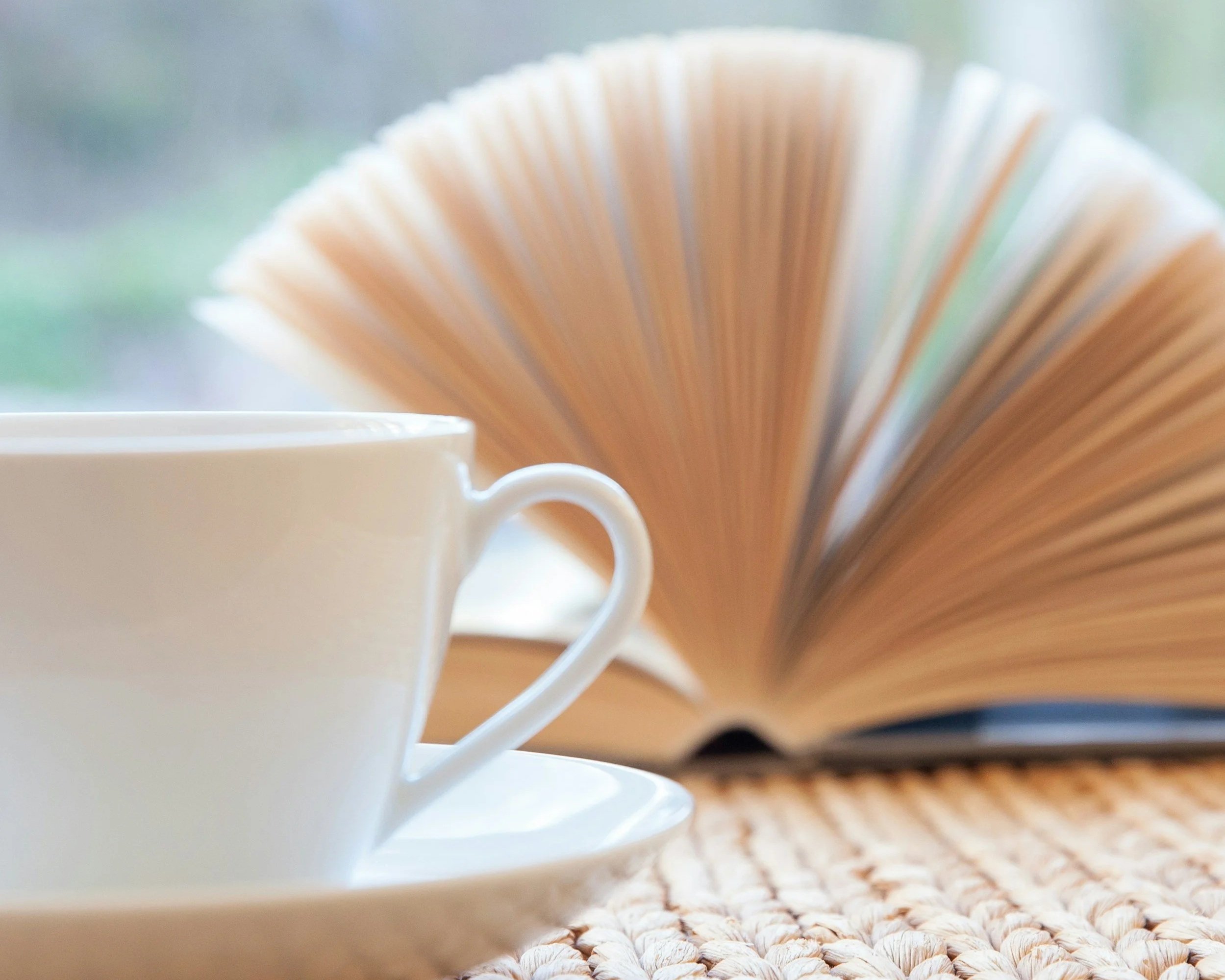 Close-up of a white teacup and fanned out book on a textured orange surface.
