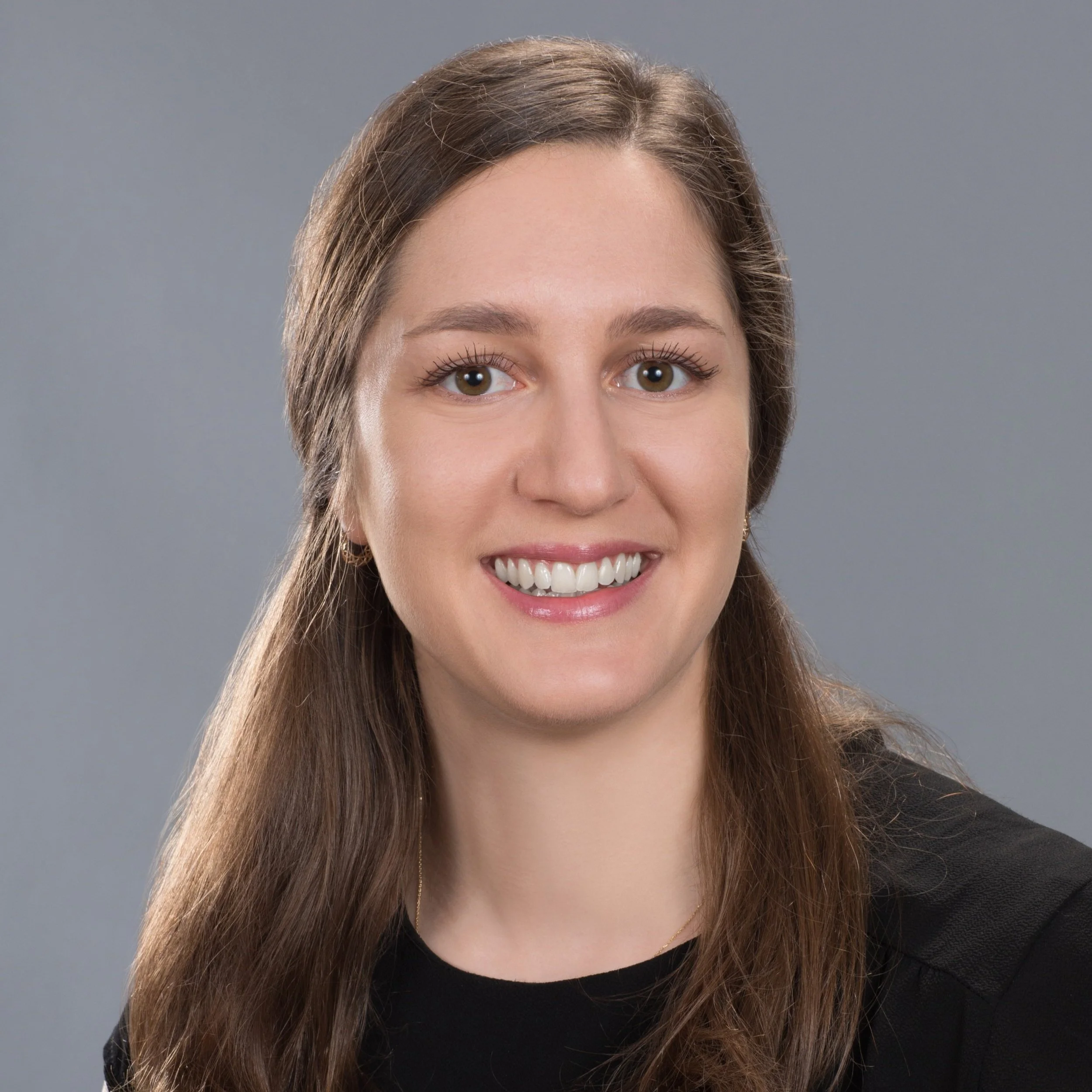 Close-up of a woman with long brown hair, smiling, against a gray background.