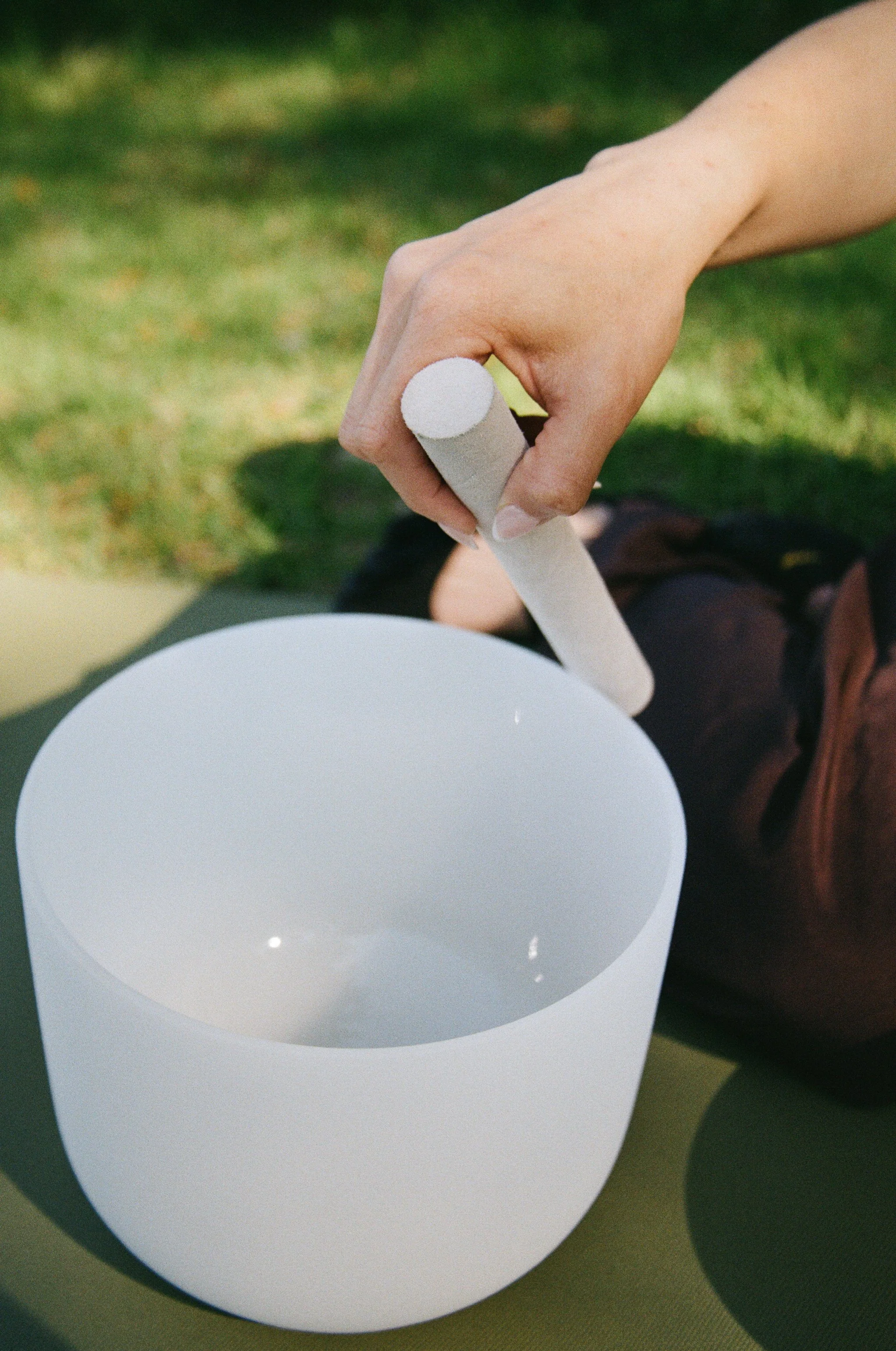 A person's hand is holding a white chalk over a cylindrical container or chalk holder, with a grassy background.