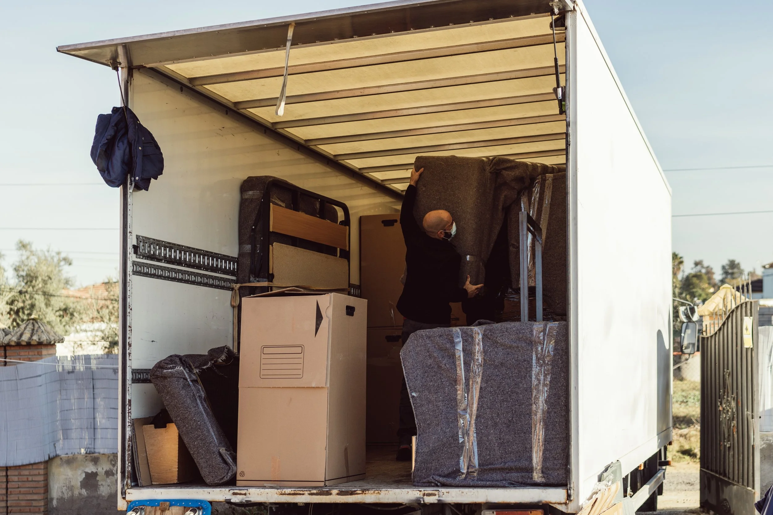 A man packing furniture into a moving truck, including large stone tiles, a cardboard box, and furniture.