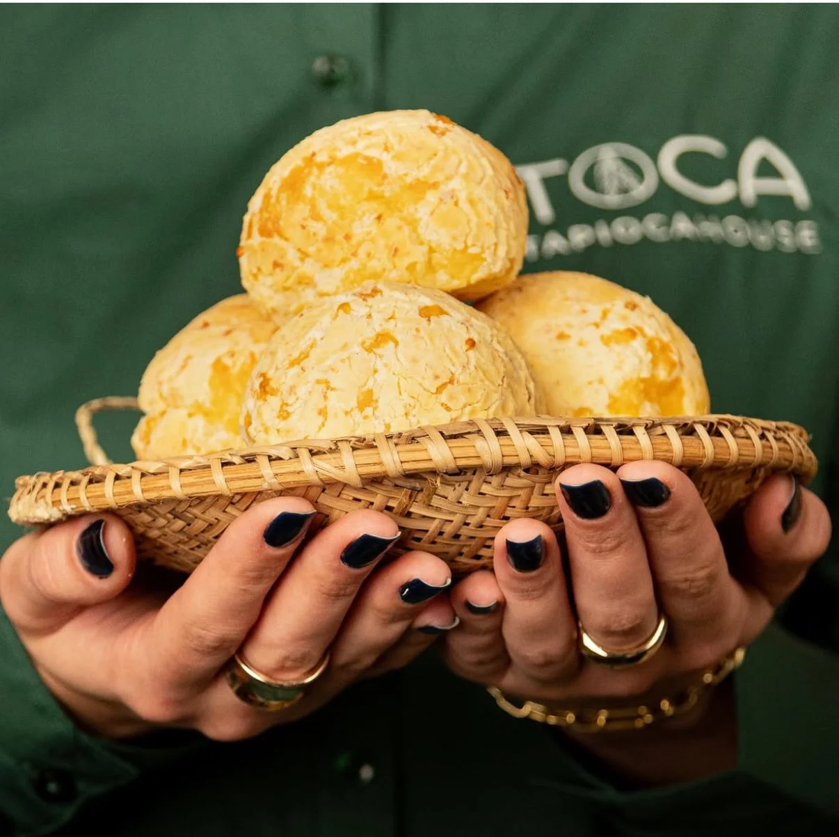 Person holding a woven basket with cheese cheese balls, with black-painted nails and rings.