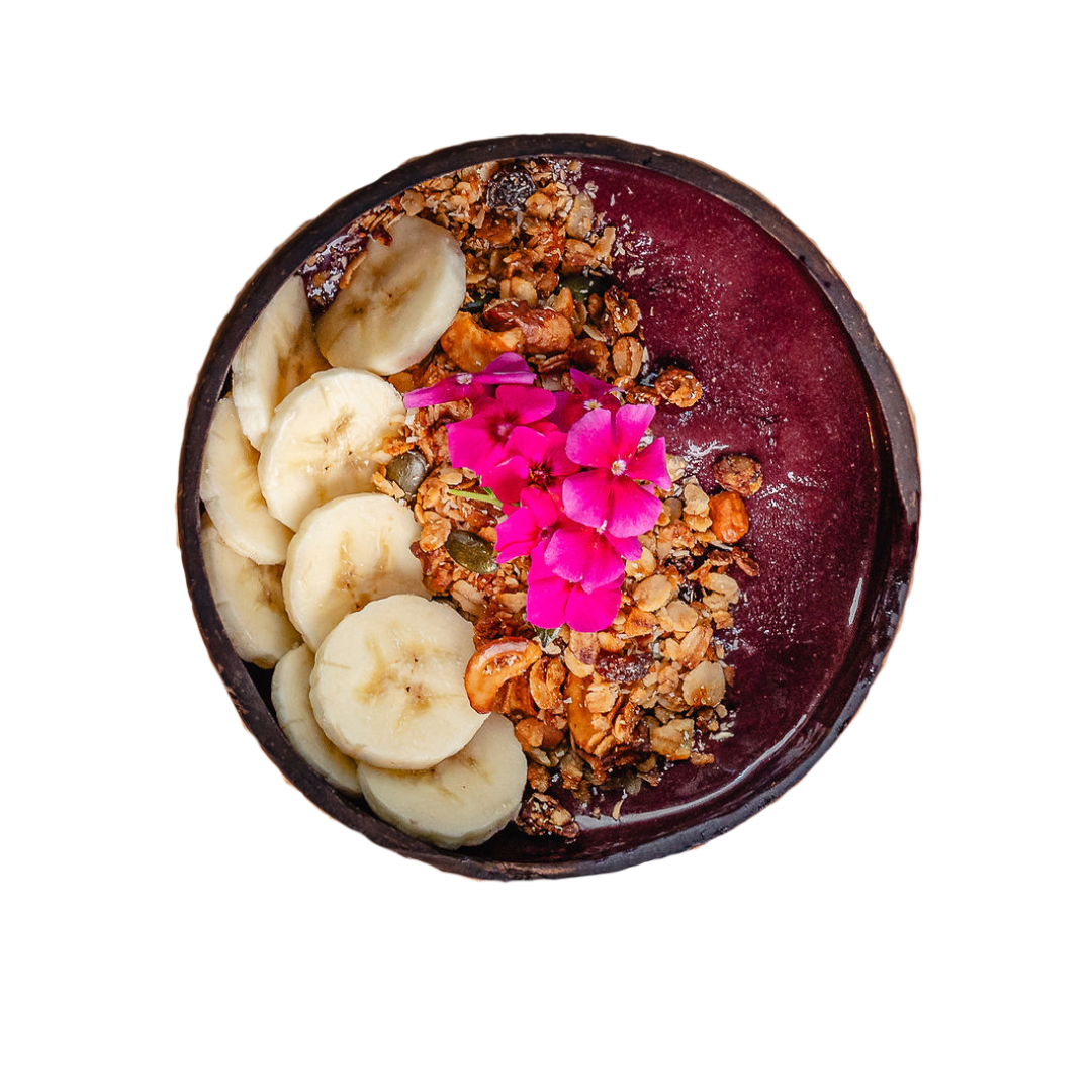 Acai bowl topped with sliced bananas, granola, pumpkin seeds, and bright pink edible flowers.