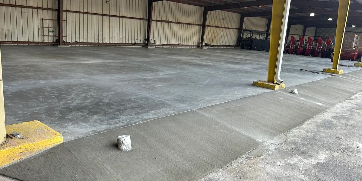Empty indoor parking lot with freshly poured concrete floor and yellow support columns.