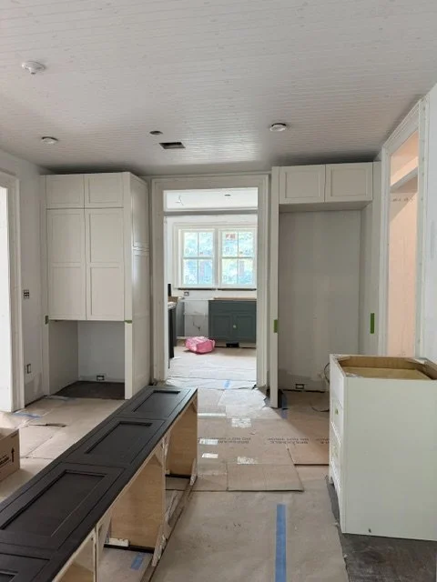 Kitchen under renovation with white cabinets, a window, and construction materials on the floor.