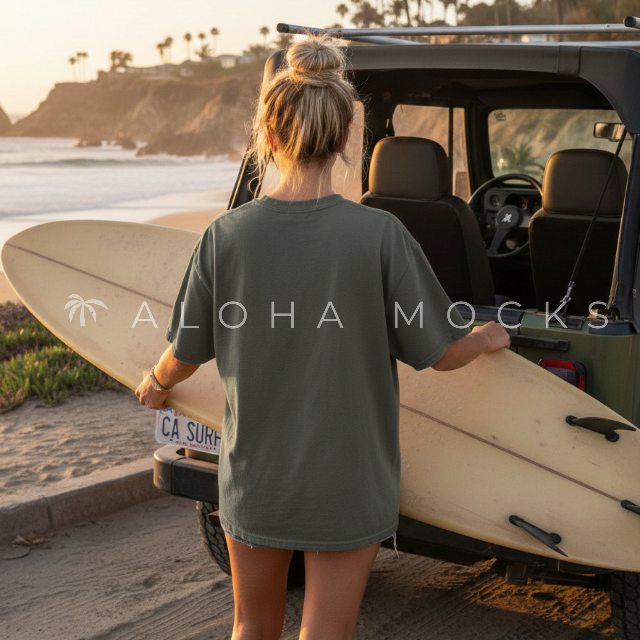 A woman with blonde hair tied up, wearing a t-shirt and shorts, holding a surfboard next to a vehicle on a beach during sunset, with palm trees and cliffs in the background.