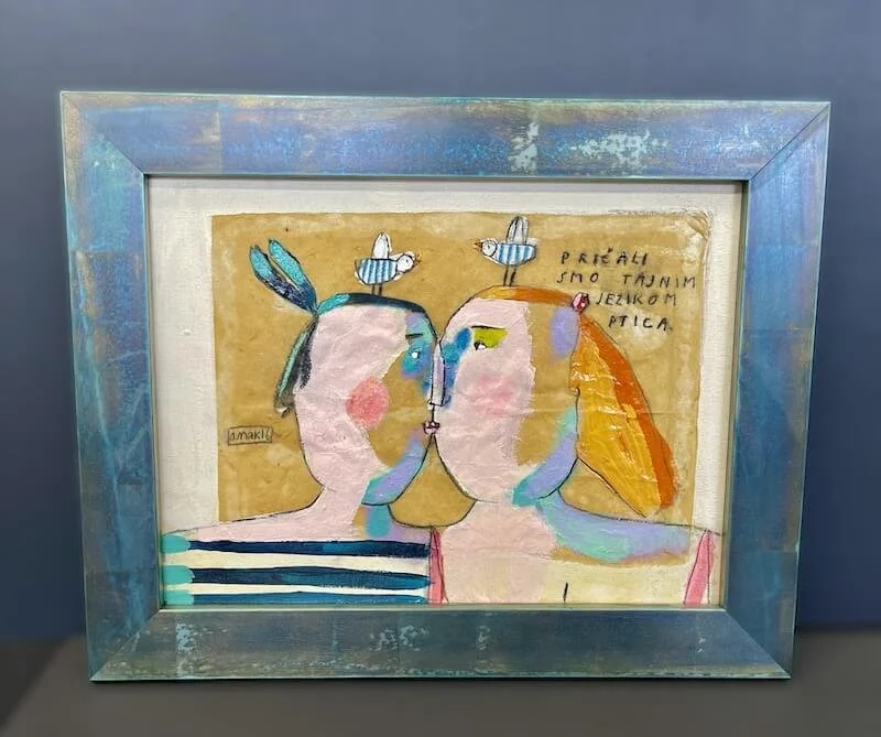 Colorful abstract painting of two faces close together, with birds on their heads, in a silver frame.
