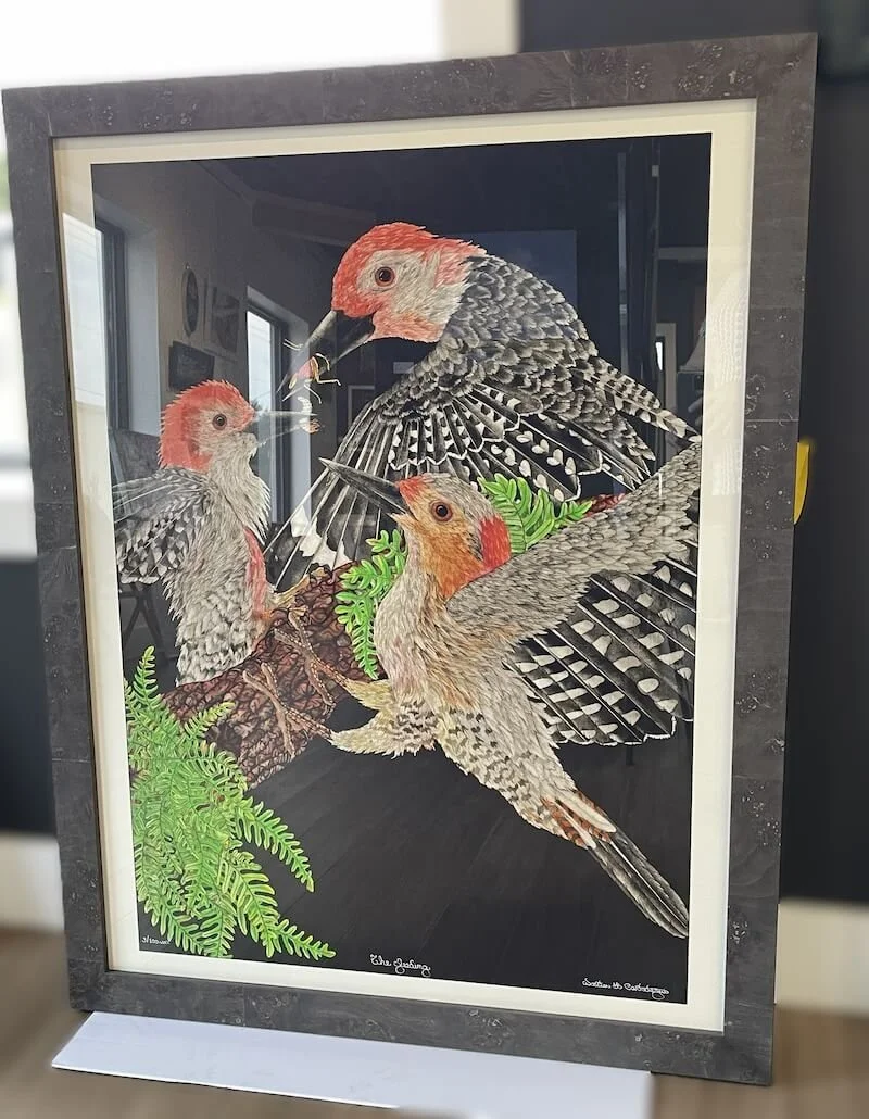 A colorful painting of three woodpeckers on a tree branch with green leaves, set in a gray frame.