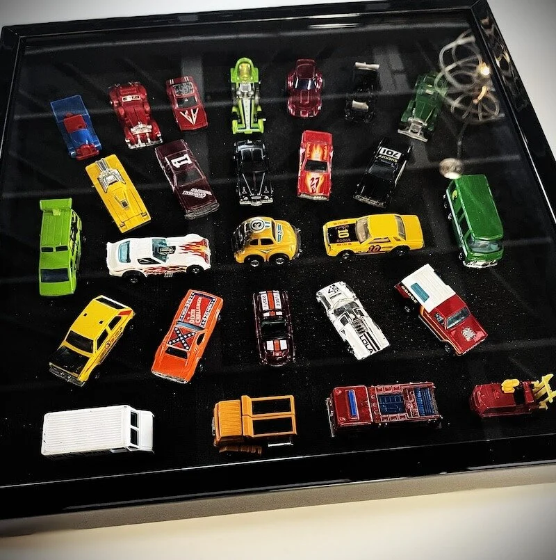 A collection of small toy cars and vehicles inside a black display case.