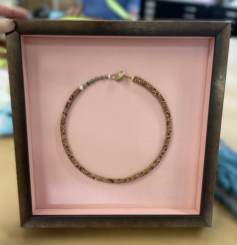 Necklace with small beads and a larger, decorative clasp, displayed in a pink-lined display box.