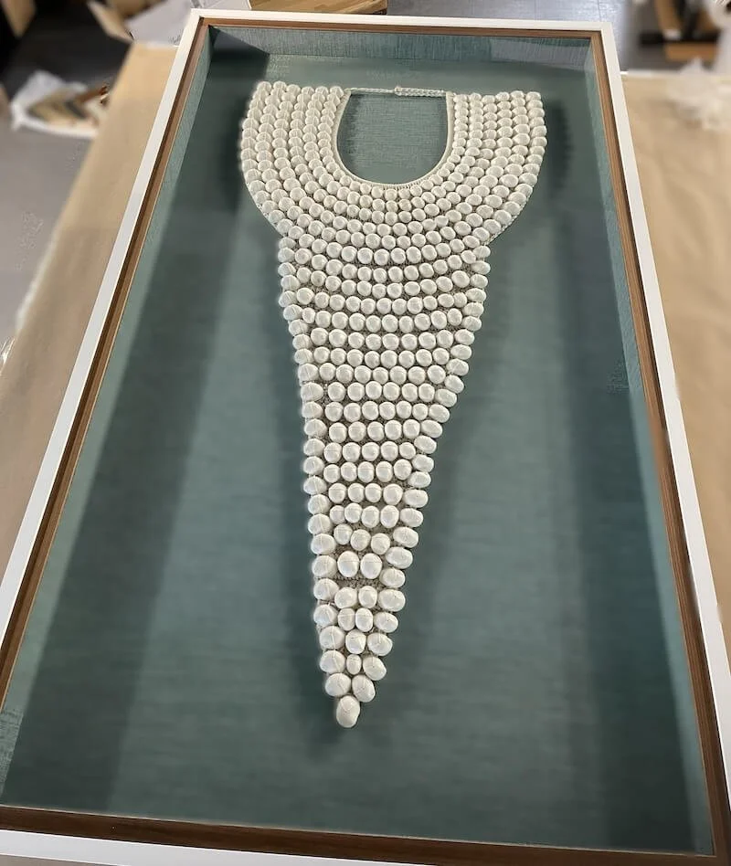 A display case contains a large arrangement of white golf balls arranged in a pattern resembling a necklace or collar.