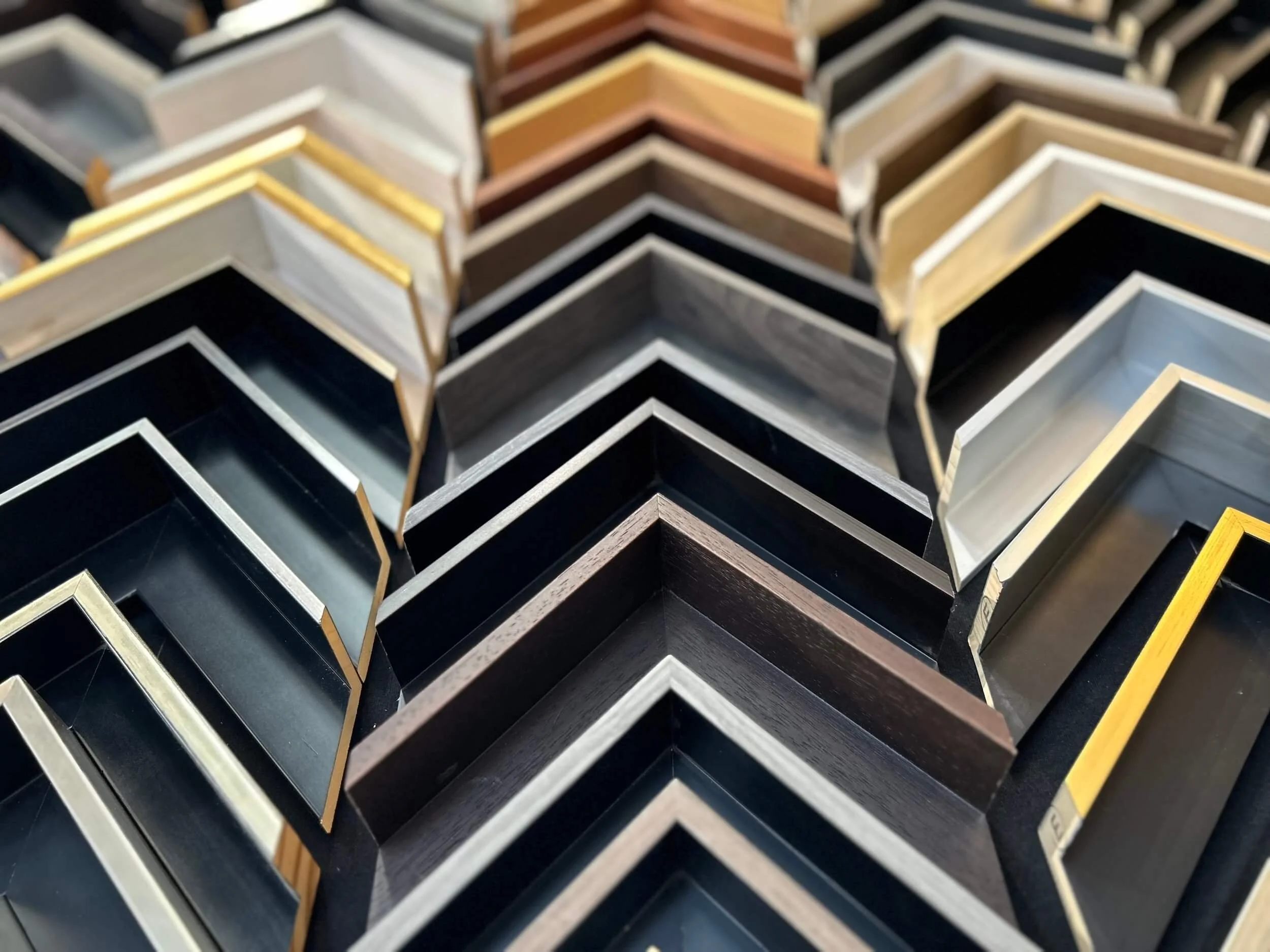 Multiple picture frames in various colors and finishes are stacked in a display, arranged in a grid pattern.