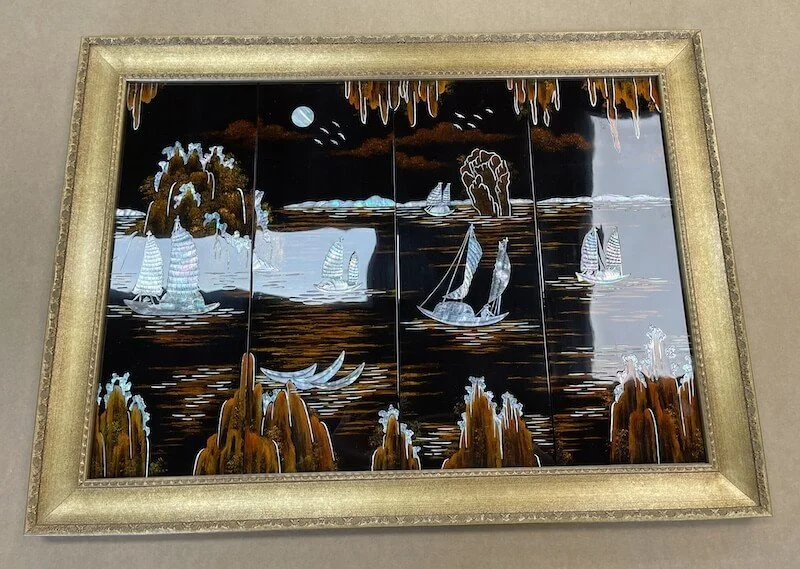A framed artwork depicting ships sailing on a body of water at night, with trees and a full moon in the sky.
