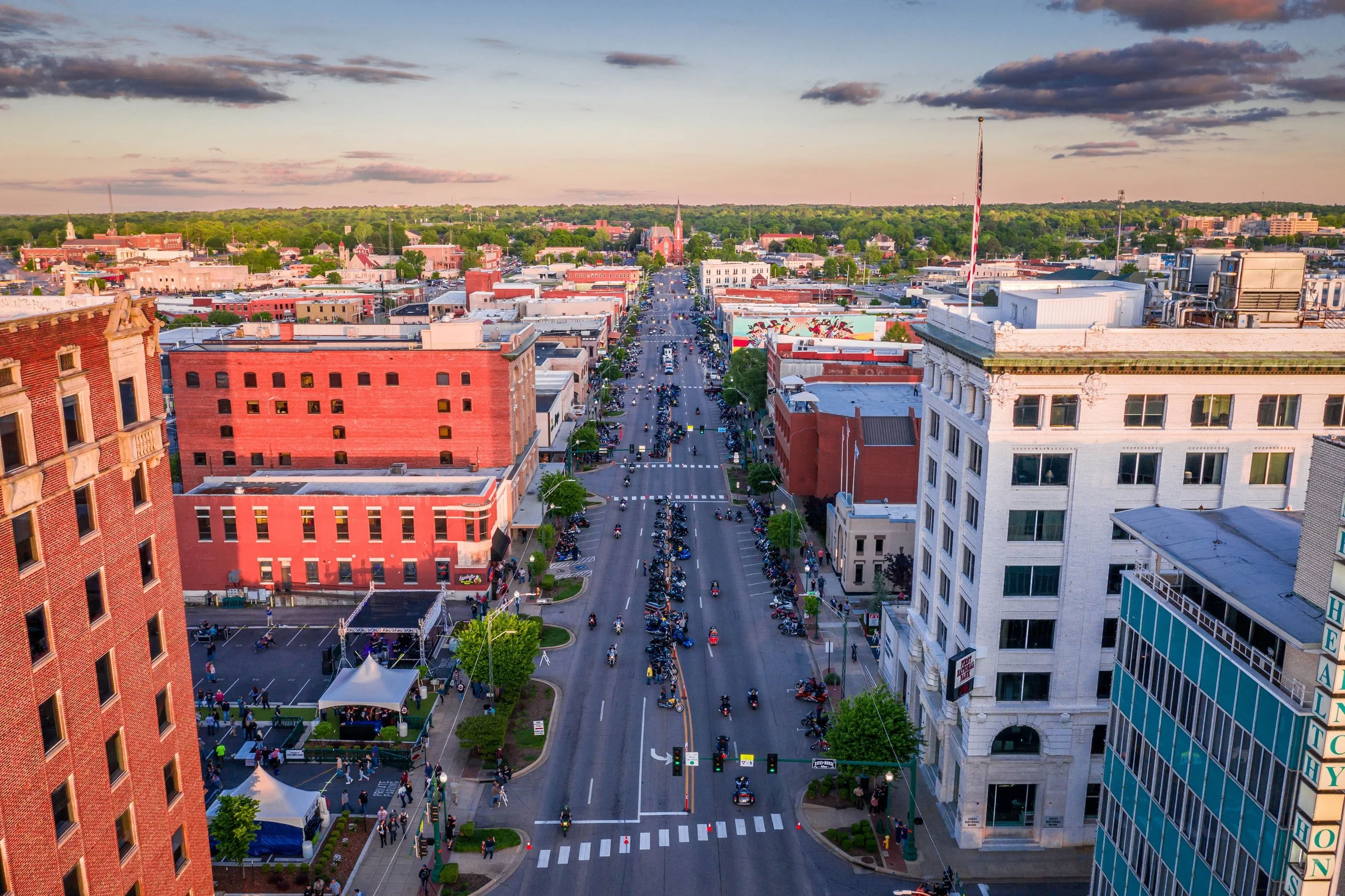 Fort Smith, Arkansas, Aerial view of a city street with cars and motorcycles, surrounded by buildings and trees, during sunset with a colorful sky.