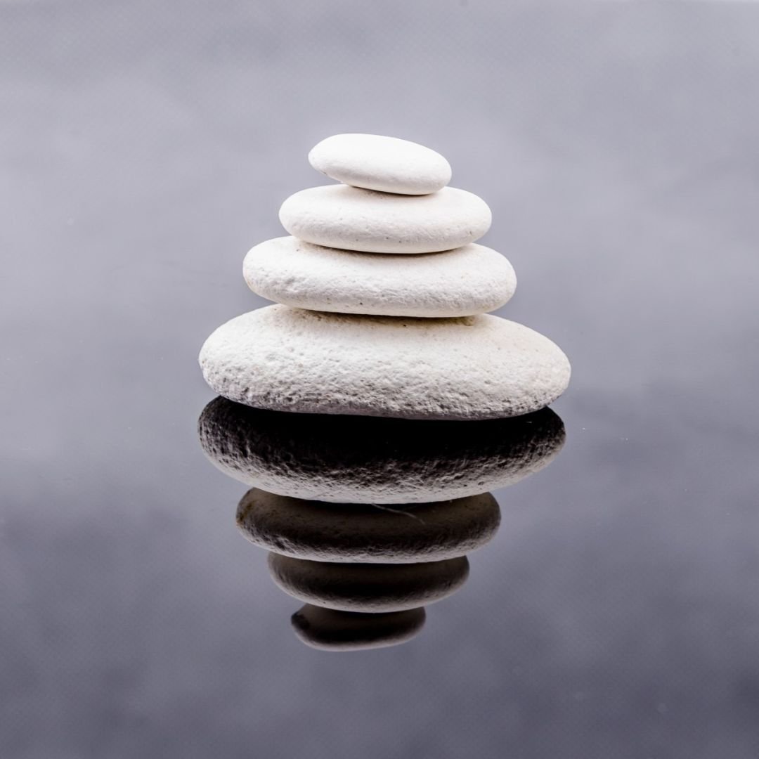 Four white porous stones stacked from largest to smallest on a dark, reflective charcoal surface creating a balanced yin-yang aesthetic for a foundational virtual Usui Reiki Level 1 training.