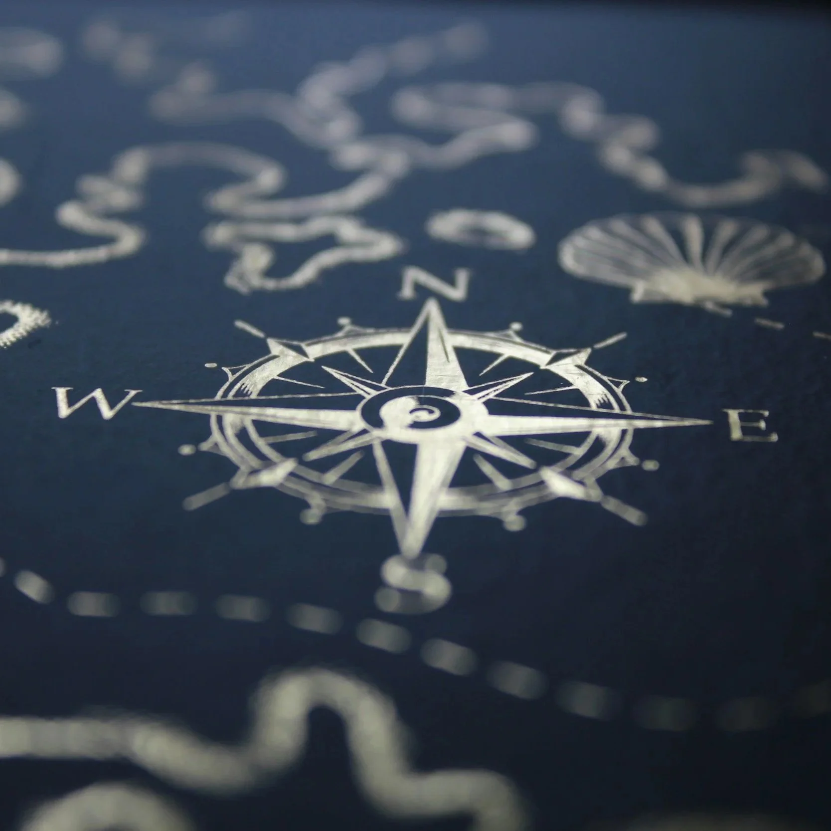 Close-up, angled view of a golden printed compass rose on a dark charcoal gray paper background, symbolizing cosmic alignment and spiritual navigation for a destiny reading session.