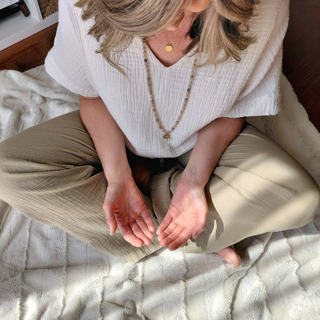 High angle view of Reiki teacher Claire sitting cross-legged on a cream blanket with open palms in a receiving gesture, representing the integrity of the energy channel.