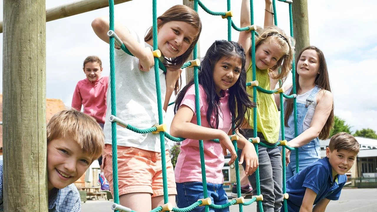 Group of children playing on a climbing net at a playground outdoors.