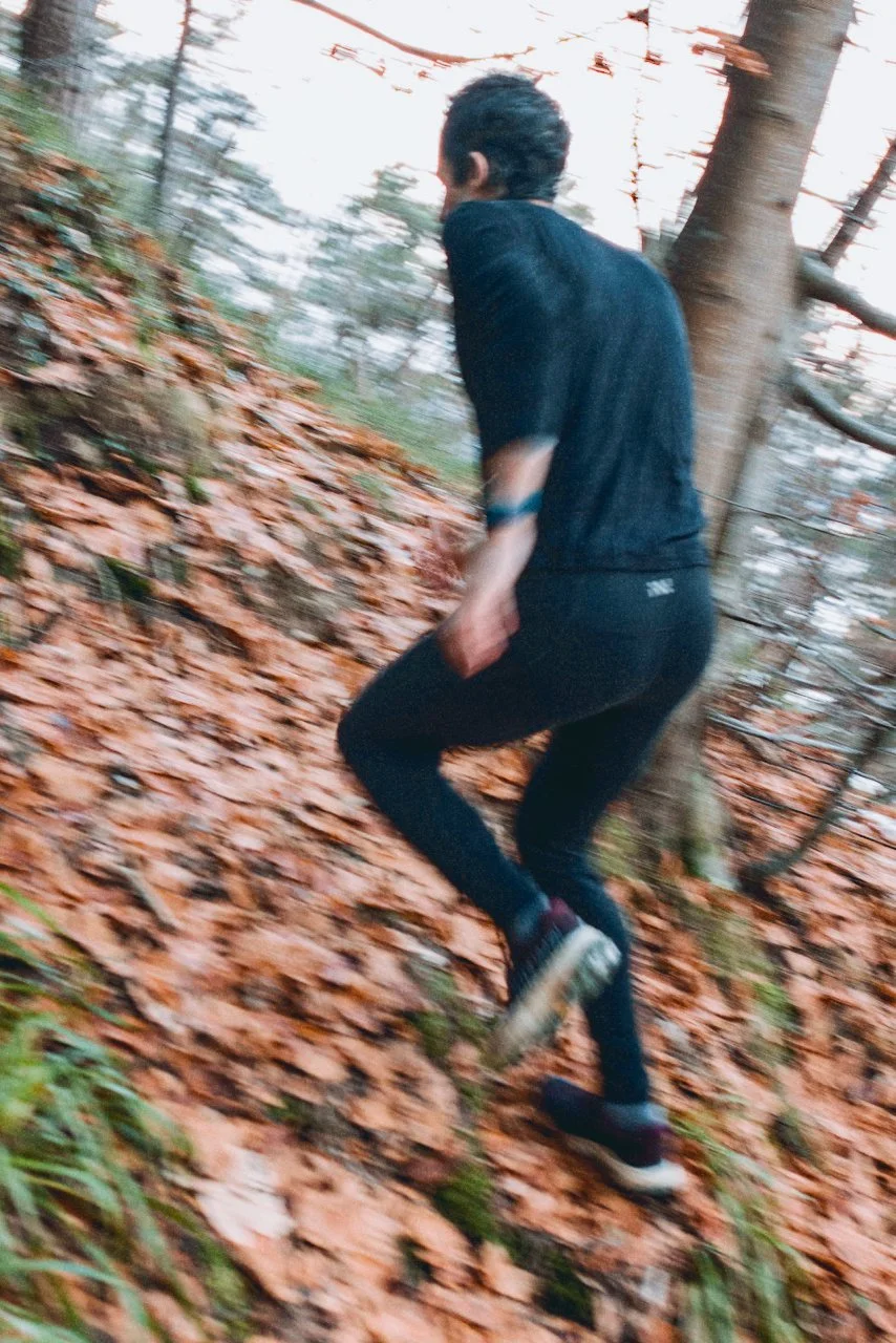 Kilian Jornet running on a trail covered in fallen autumn leaves in a forested area.