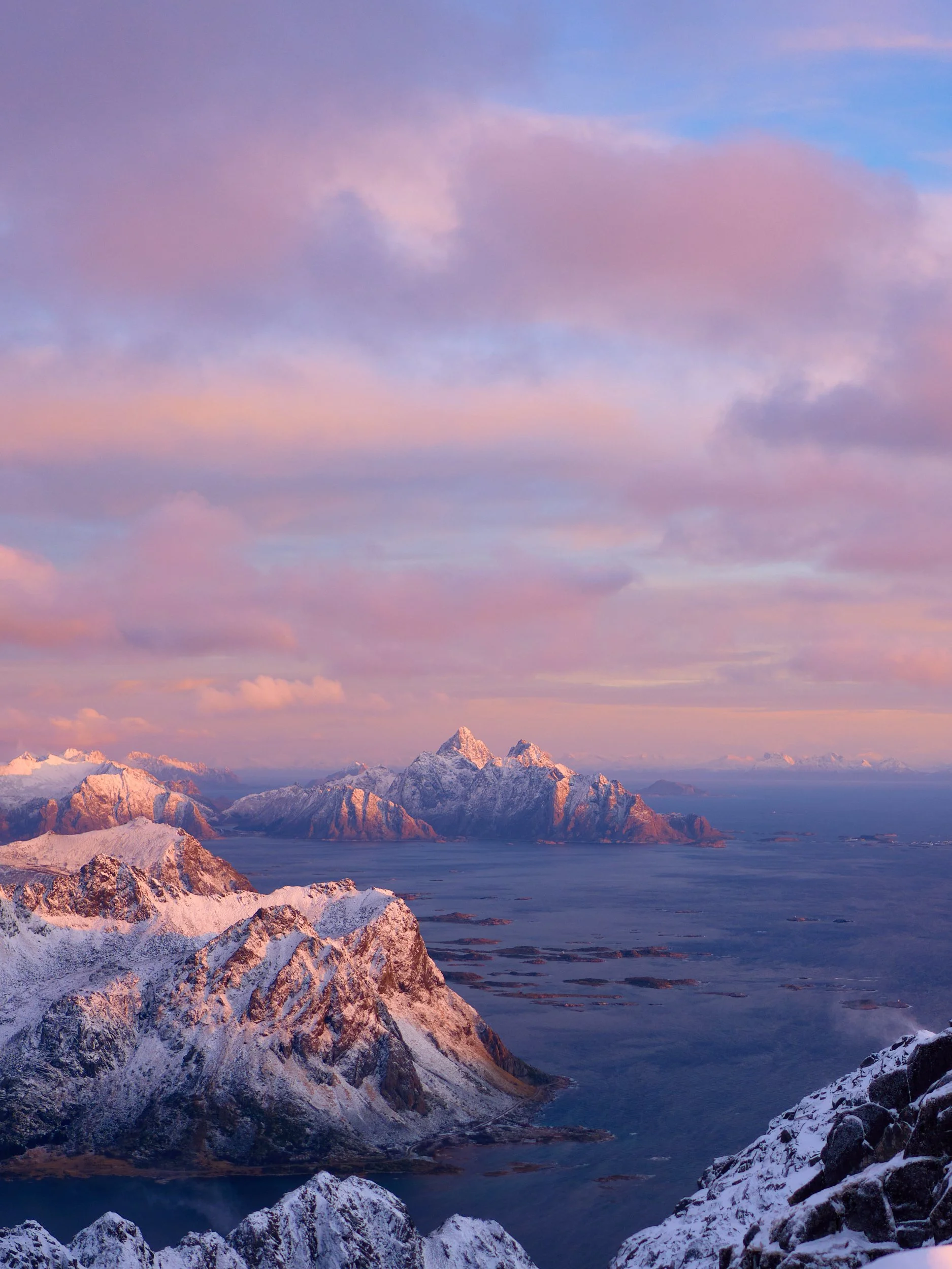 Scenic view of snow-capped mountains and islands during sunset with pink and purple clouds in the sky.