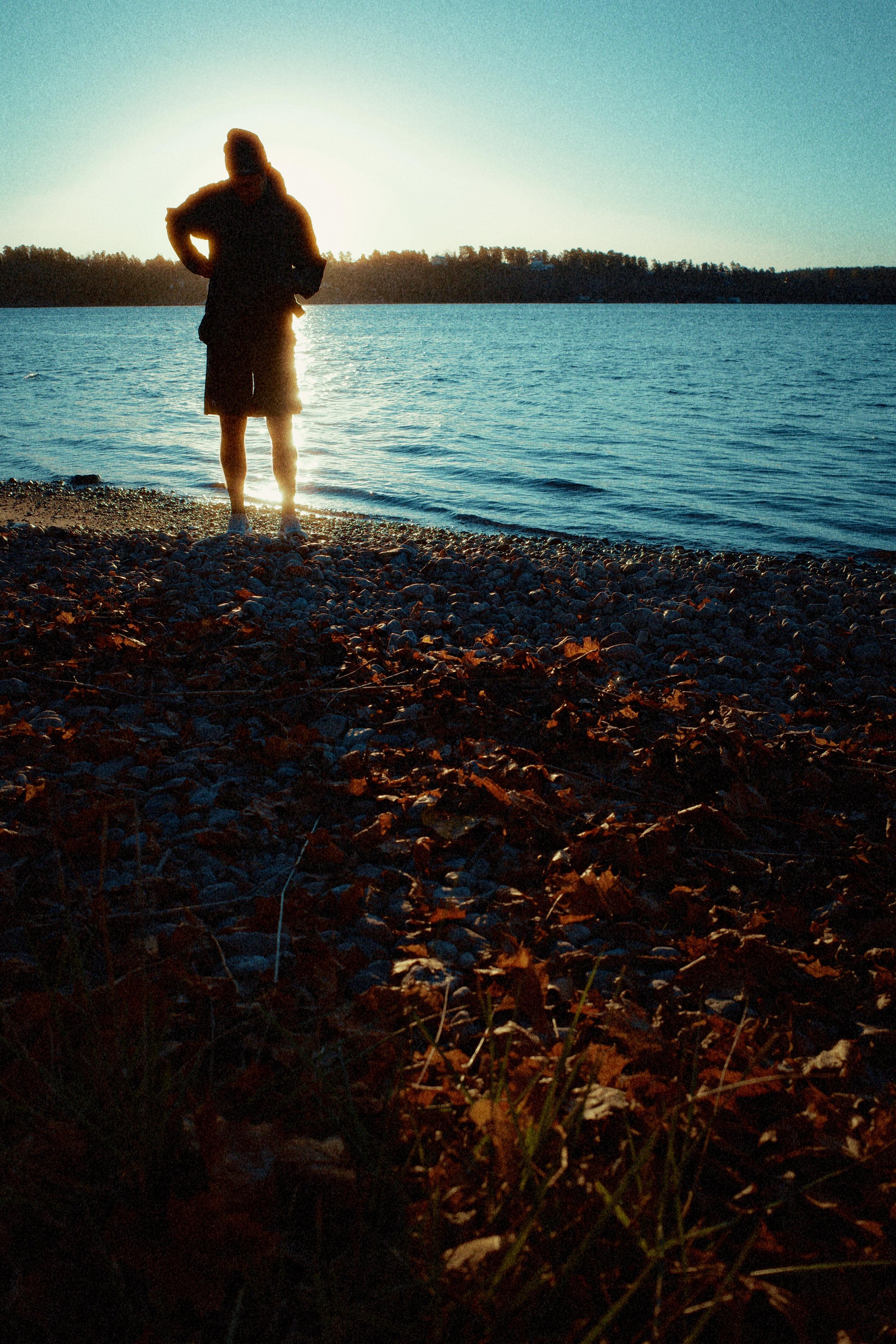 A person standing on a rocky beach near a body of water during sunset or sunrise.