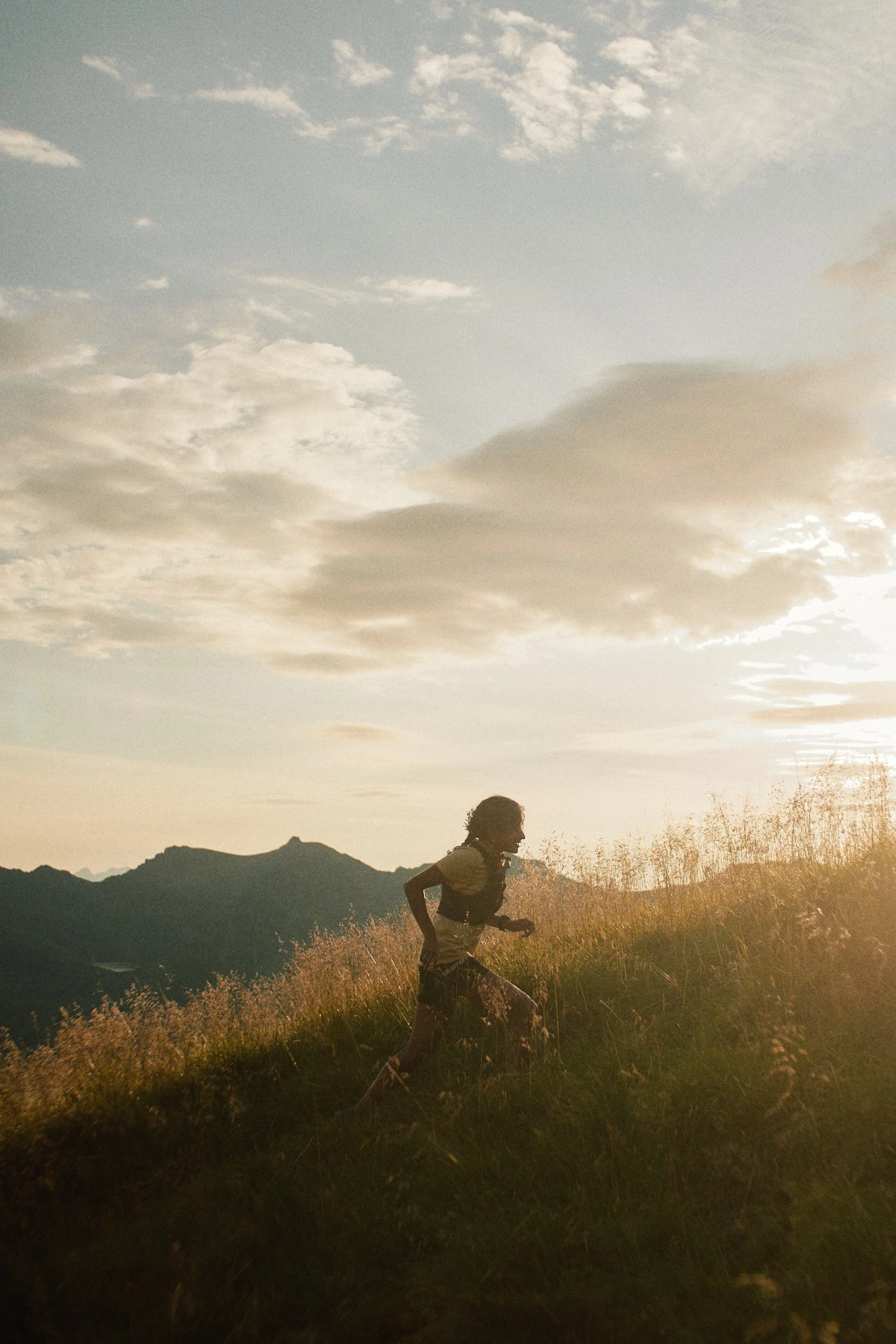 Shanga Ba running on a trail in a grassy landscape with mountains in the background during sunset or sunrise.