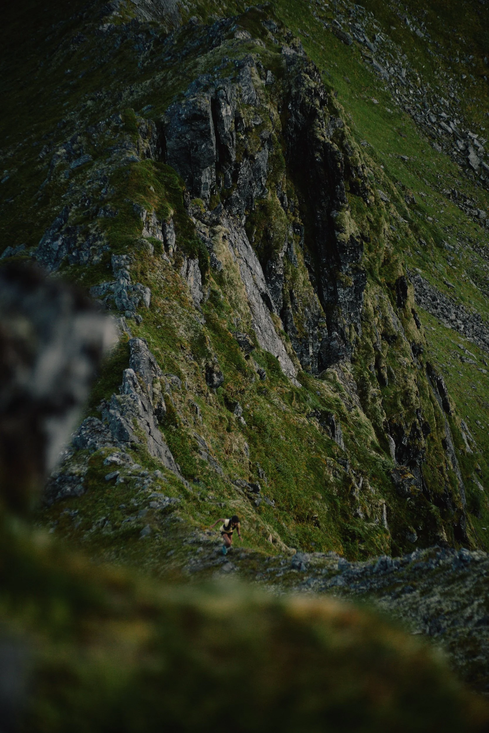 A person hiking on a rocky mountain trail surrounded by steep, moss-covered cliffs and green vegetation.