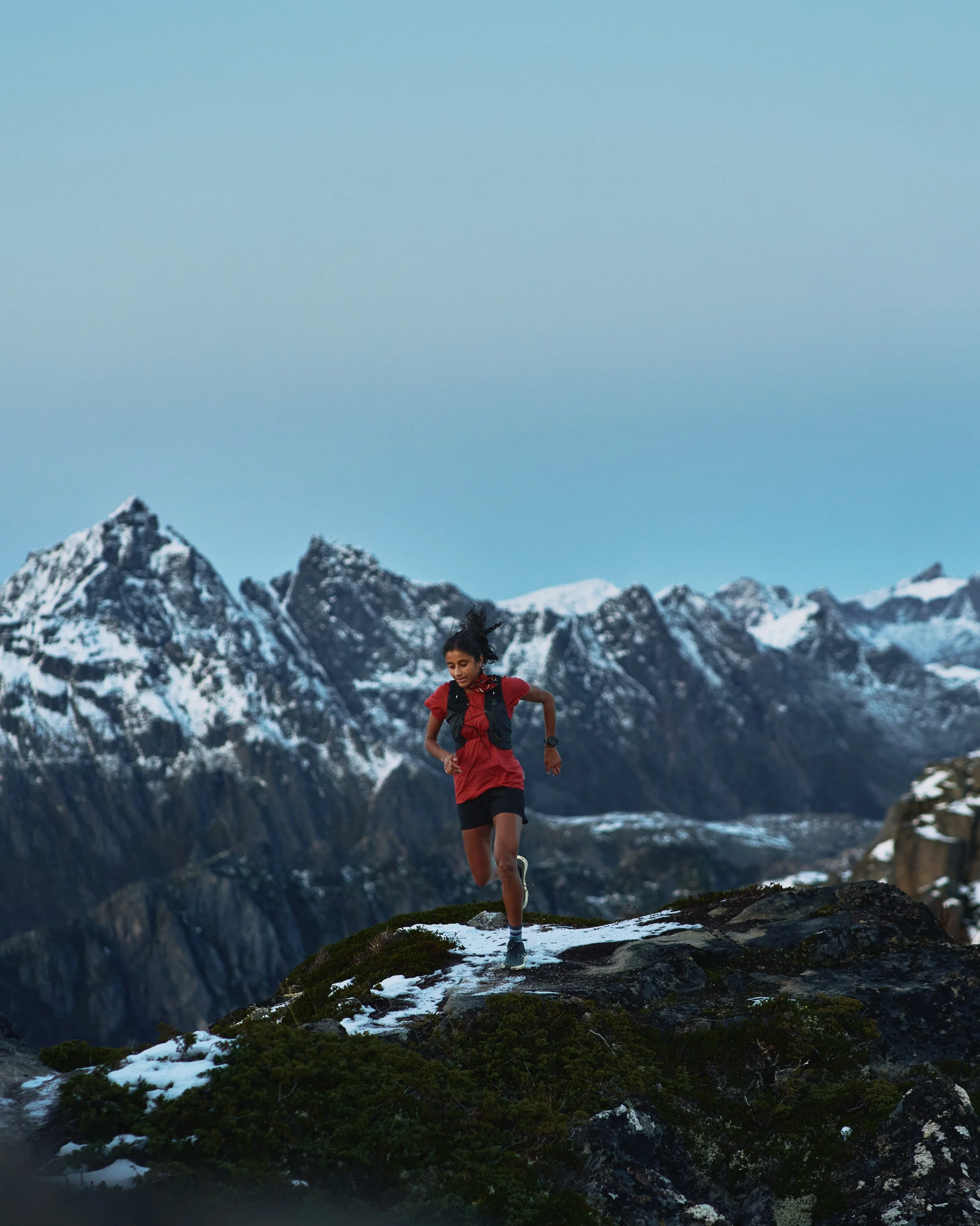 Shanga Ba running on a mountain trail with snow and mountains in the background.