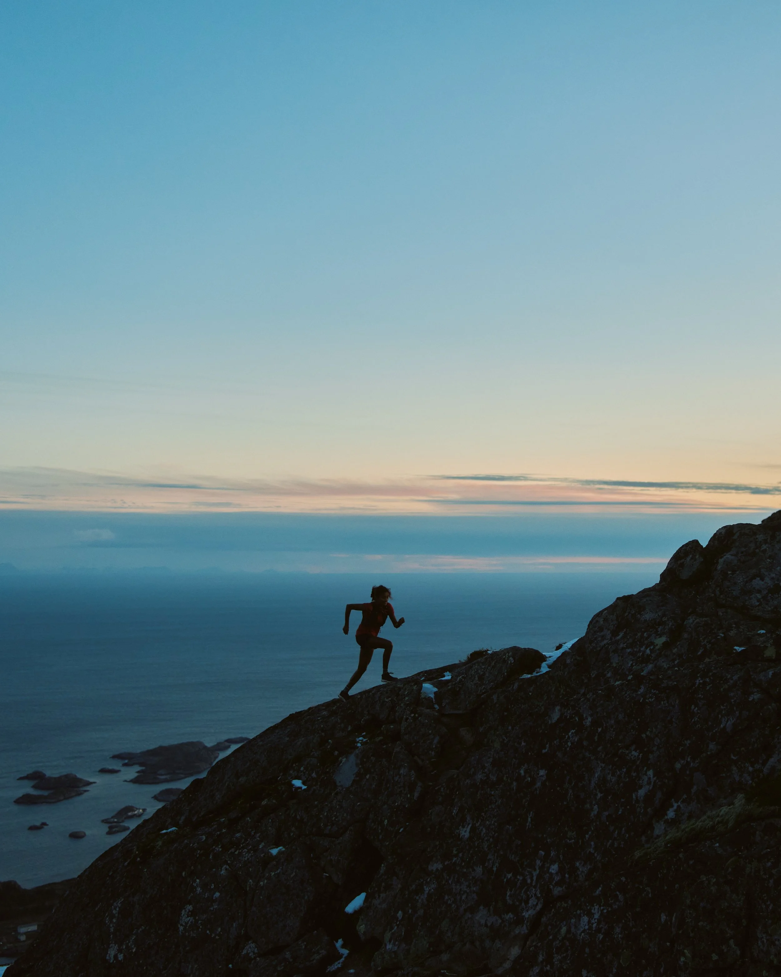 Person running on rocky hillside during sunset or sunrise over the ocean.