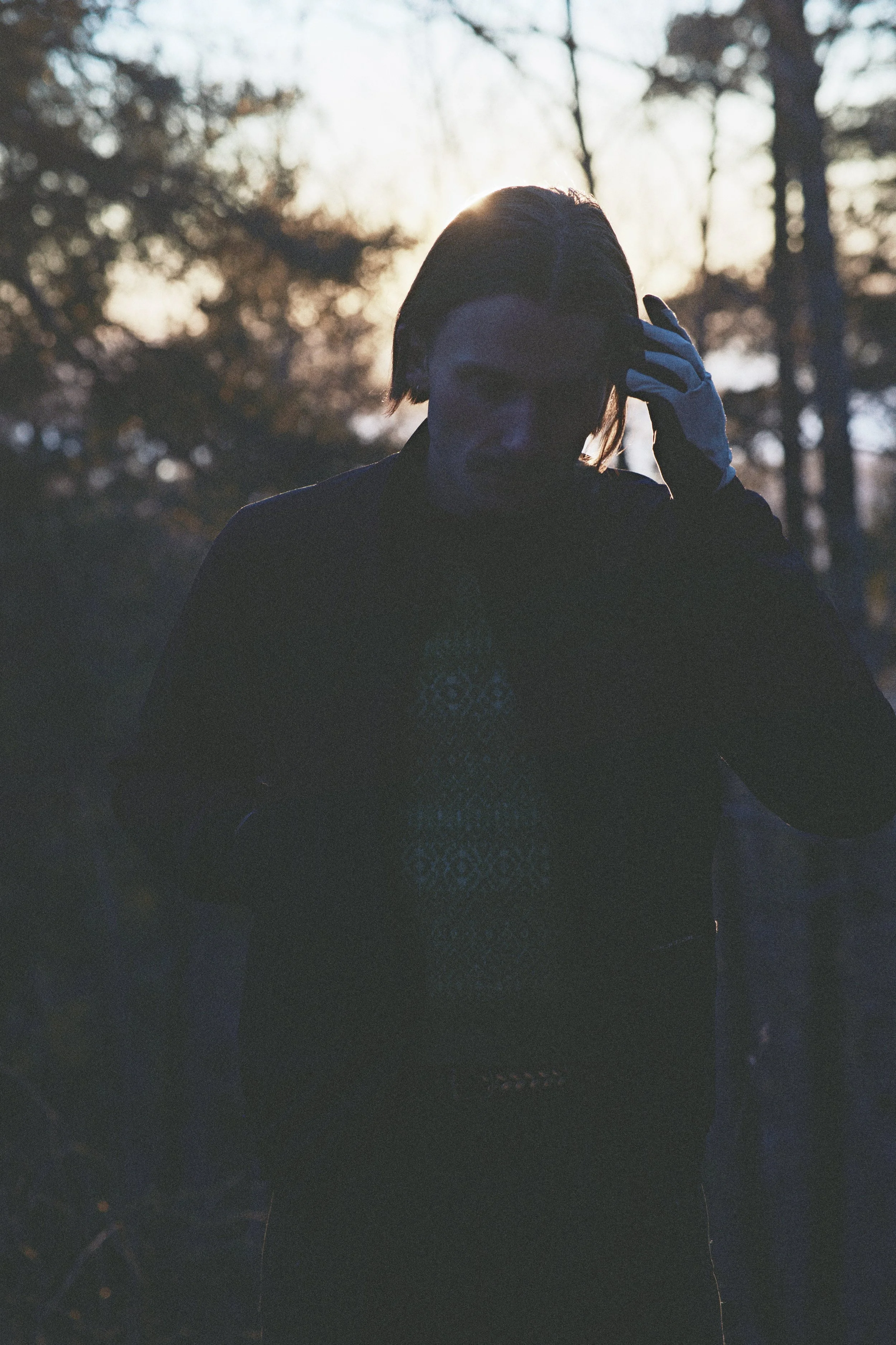 Patrick Stangby with short dark hair, wearing a dark outfit and a white glove, standing outdoors during sunset or dusk, with trees in the background.