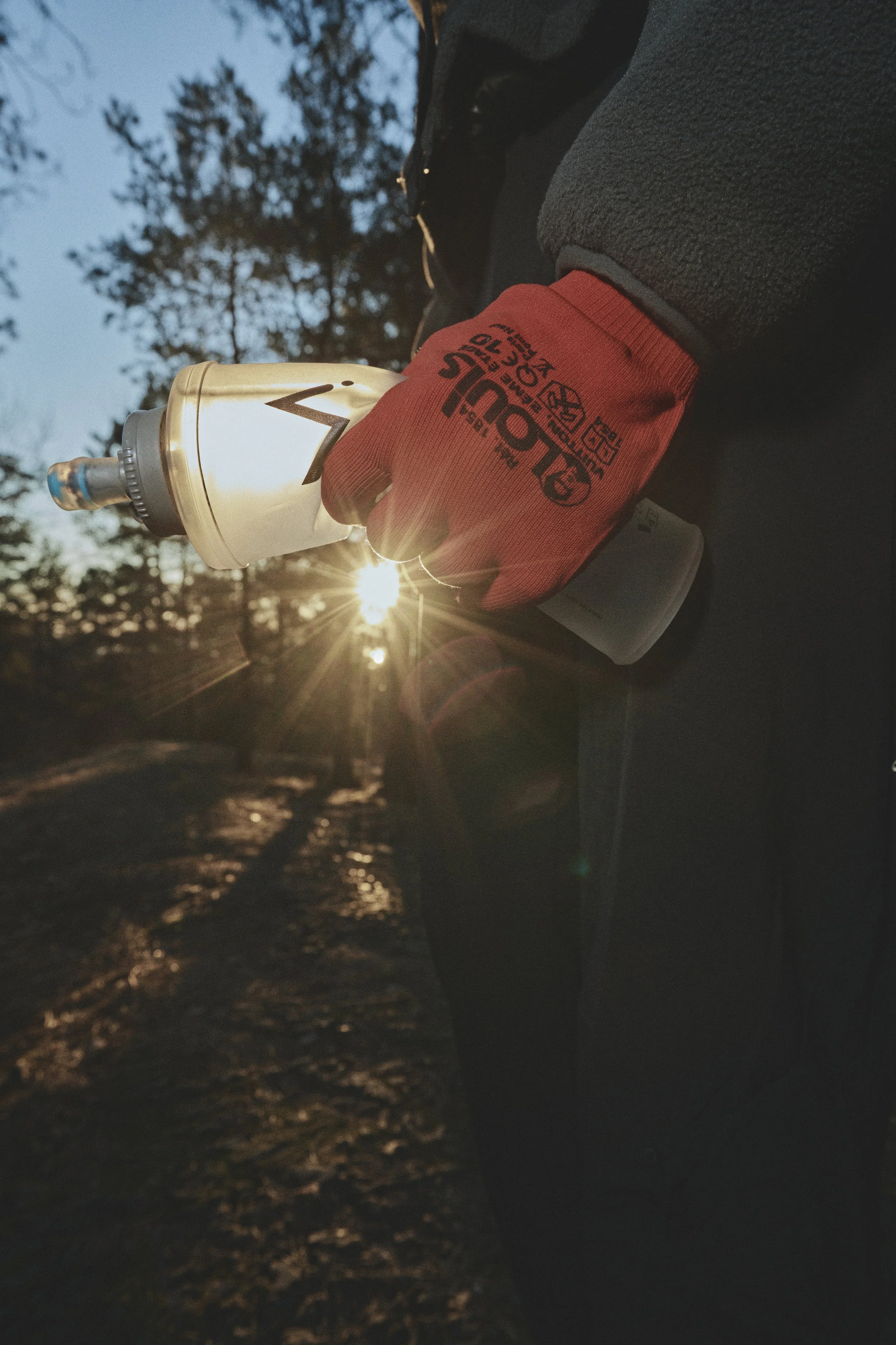 A person wearing red gloves holds a water bottle during sunset outdoors.