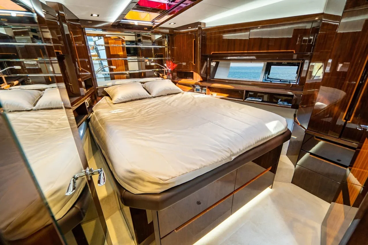 A luxurious bedroom with polished wooden walls, a large bed with a beige sheet and pillows, and a window showing the ocean outside.