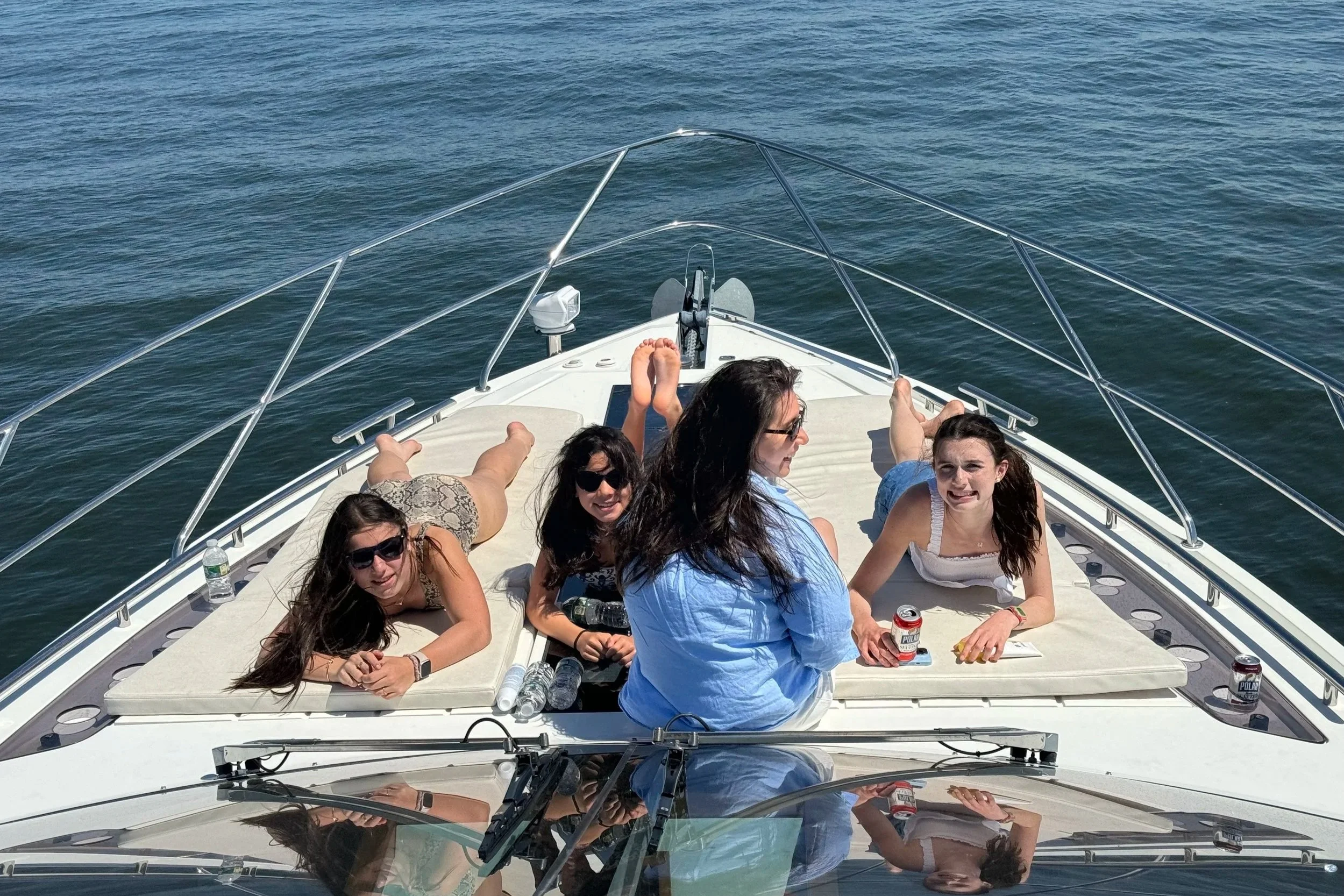 Group of people relaxing on a boat, sitting and lying on the deck, with the ocean in the background.