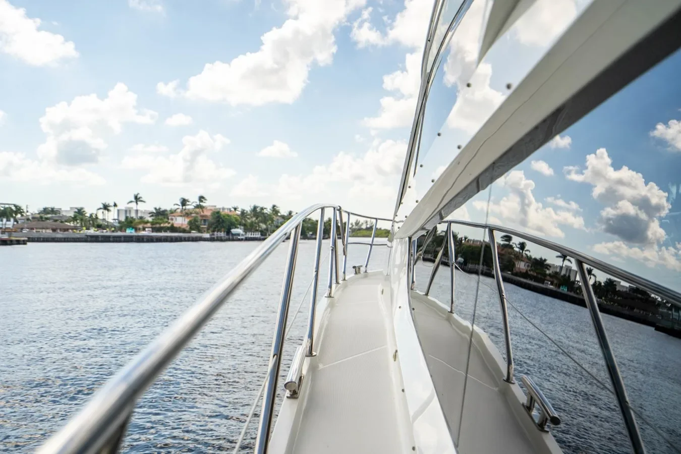 View from a boat's deck showing water, a shoreline with houses and palm trees, and a partly cloudy sky.