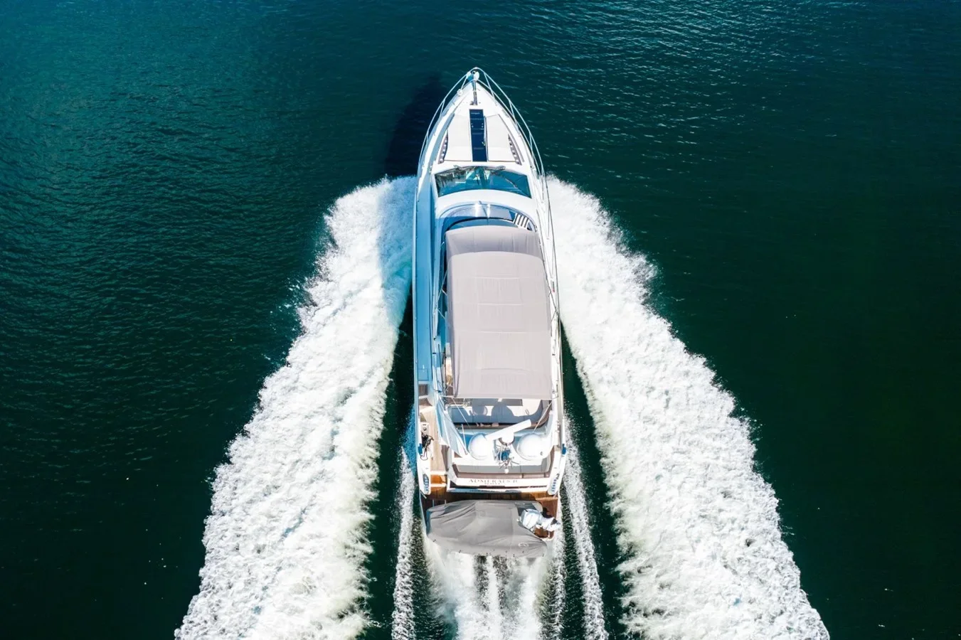 Aerial view of a white luxury yacht cruising on deep blue water, creating a wake behind it