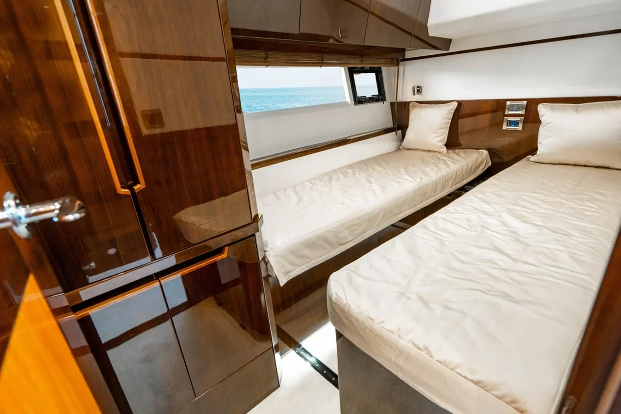 A small bedroom with two single beds, wooden accents, an open window showing the ocean, and a view of the sea.