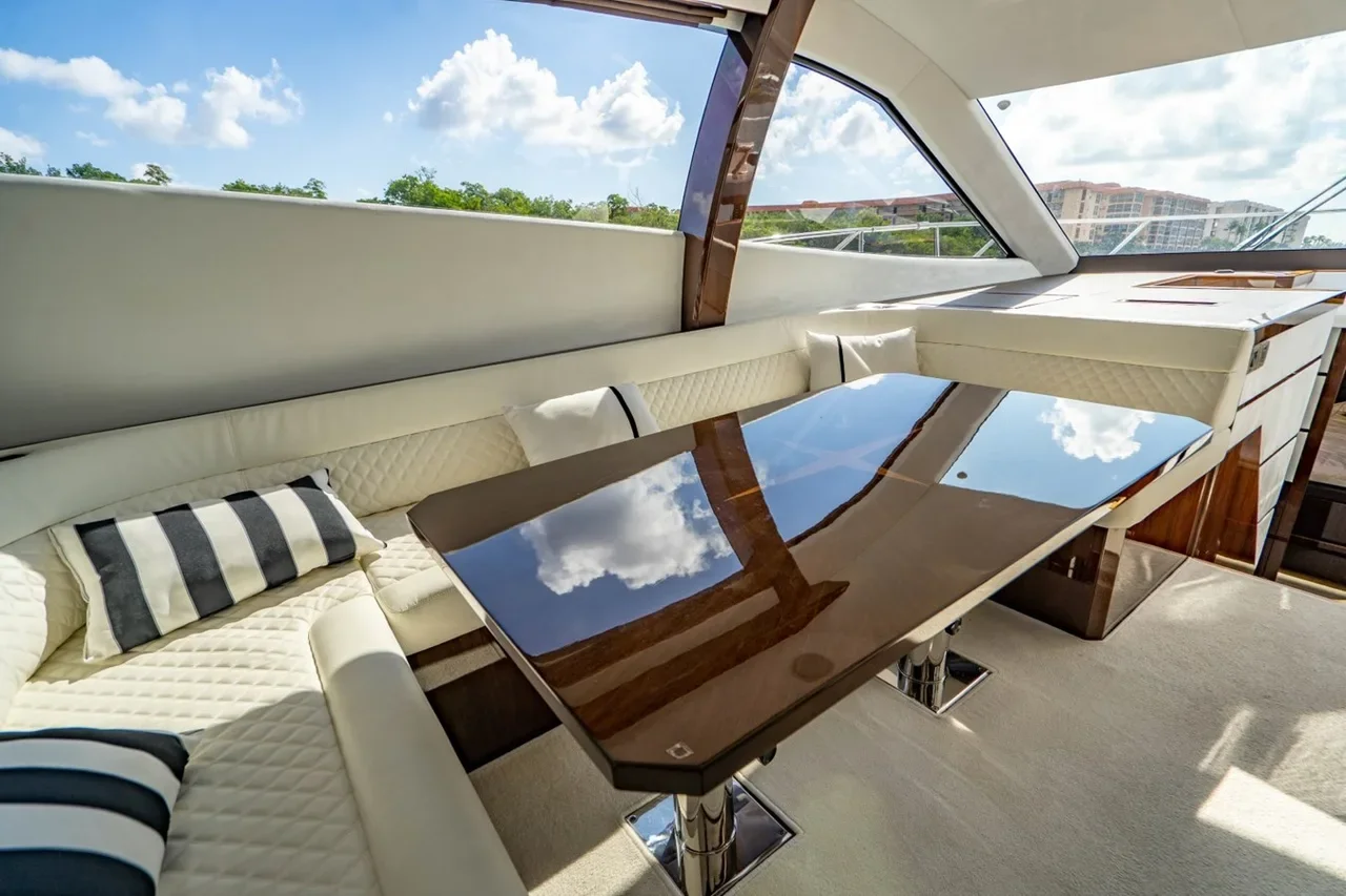 Interior of a yacht with cream leather seating, striped pillows, and a glossy wooden table, overlooking a cloudy sky and buildings outside.