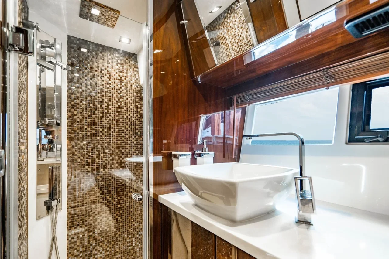 Luxurious bathroom with a walk-in shower featuring small colored mosaic tiles, a modern square vessel sink with a chrome faucet, and a large mirror above a wooden cabinet. Bright natural light from the window illuminates the space.