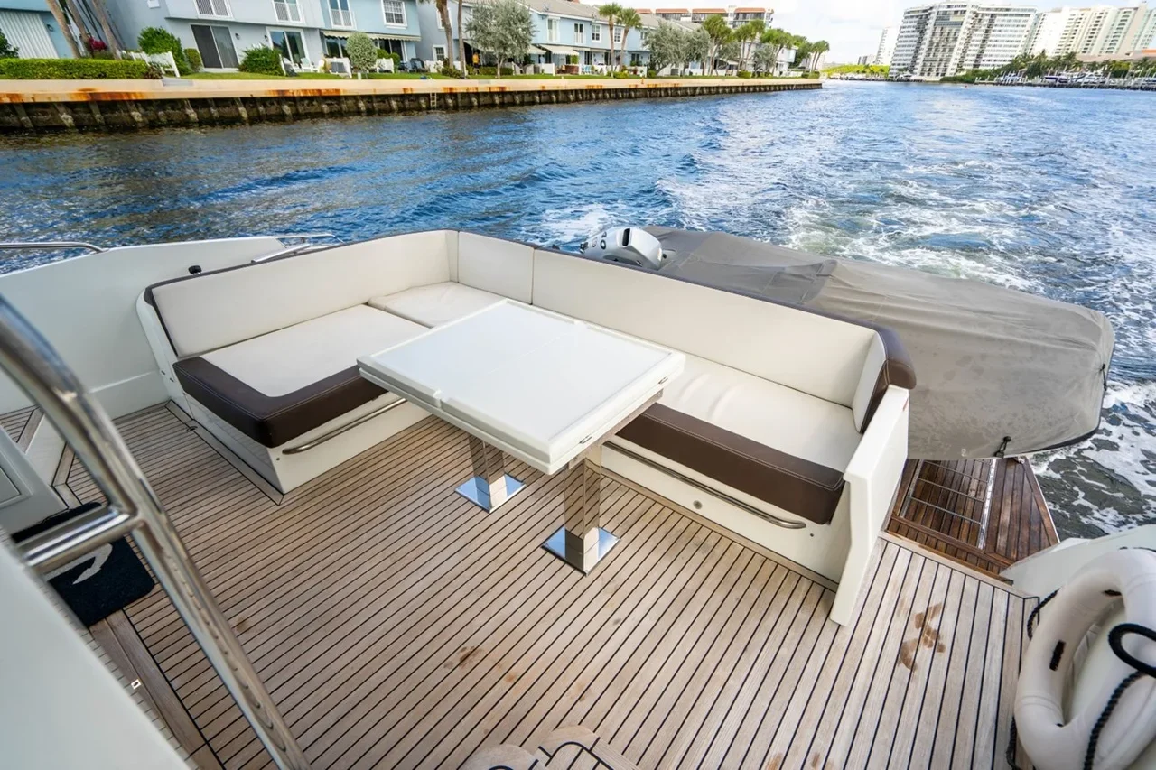 View of a boat deck with outdoor seating, a folding table, and a submerged motor, with water and buildings in the background.