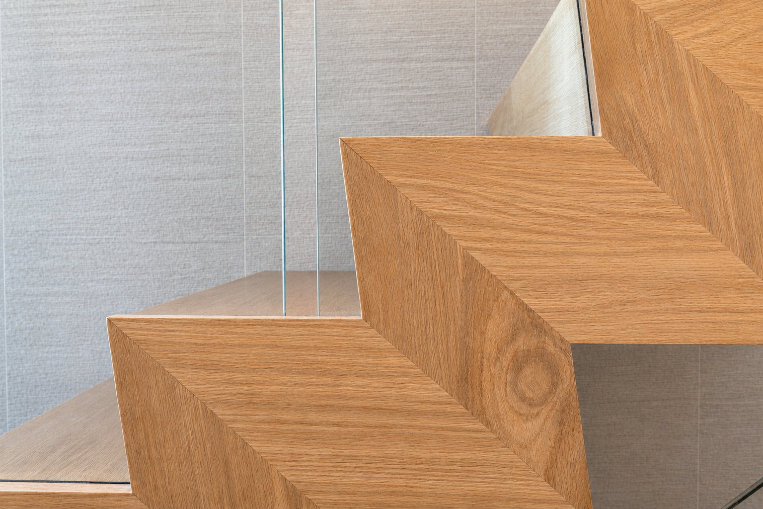 Close-up of wooden stairs with a glass railing against a beige wall.
