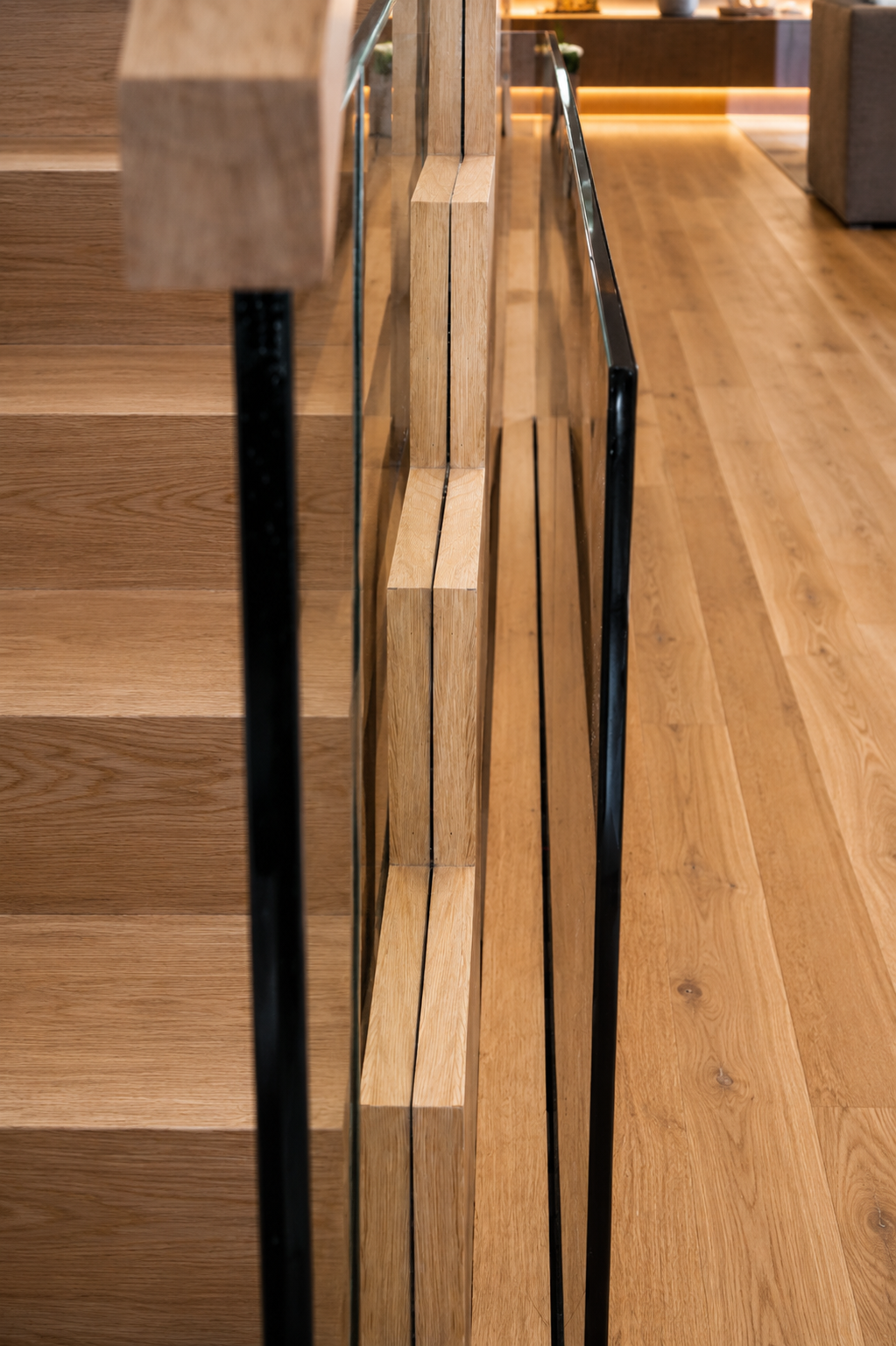 Close-up of a wooden staircase with a glass and metal railing inside a modern home or building.